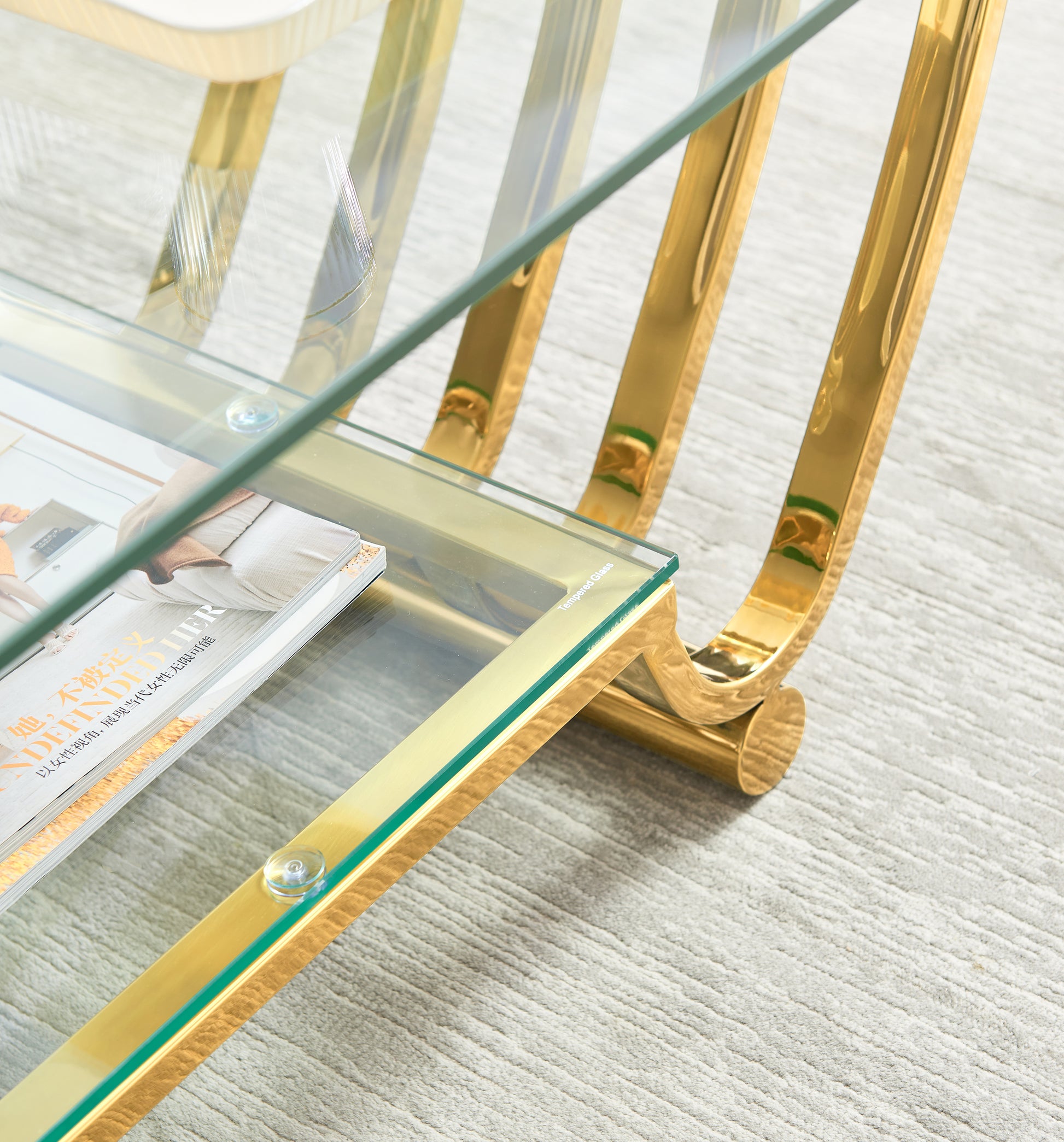 Closeup of a modern gold coffee table with a clear tempered glass top showcasing elegant curves