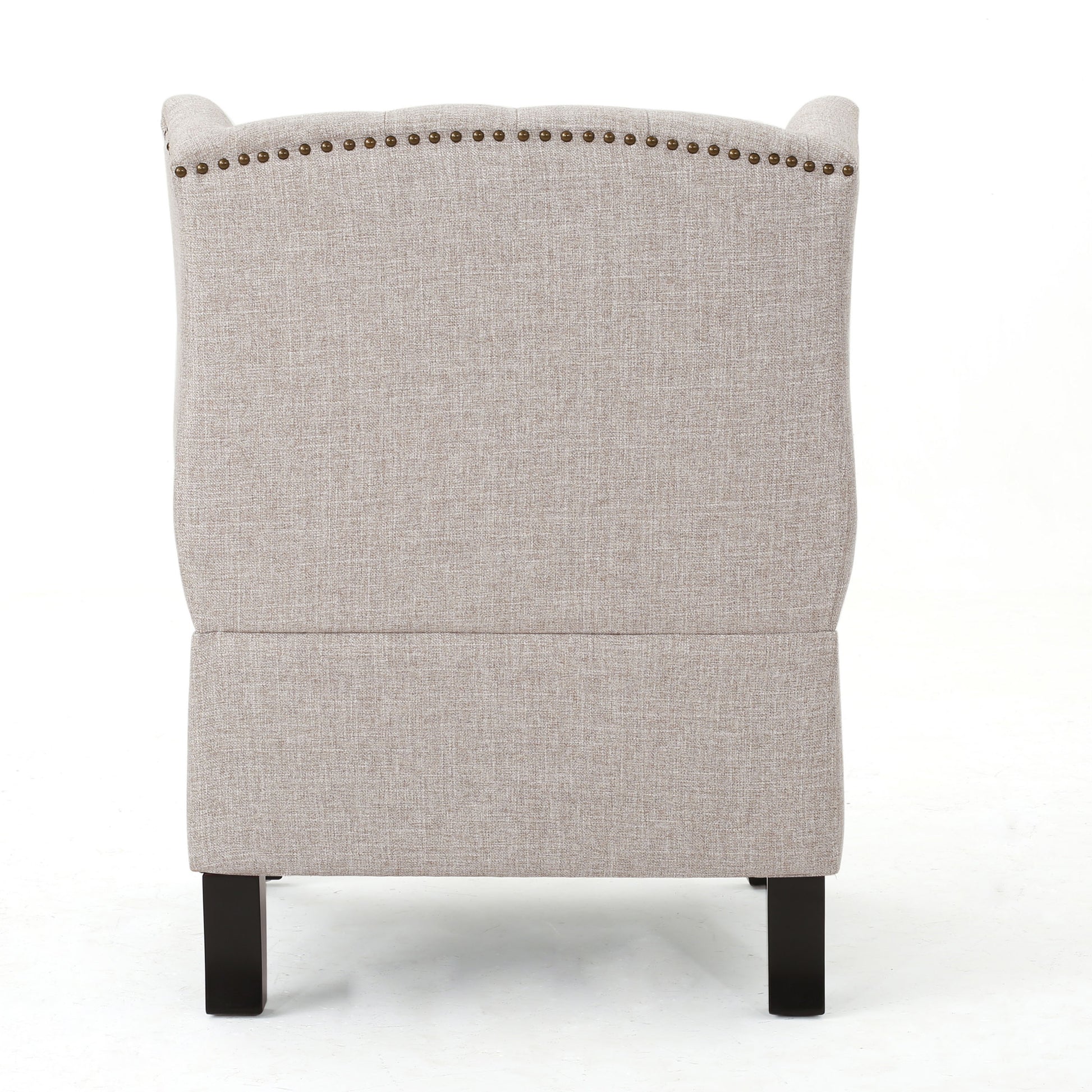 Back view of a beige upholstered wingback chair with brass nailhead trim