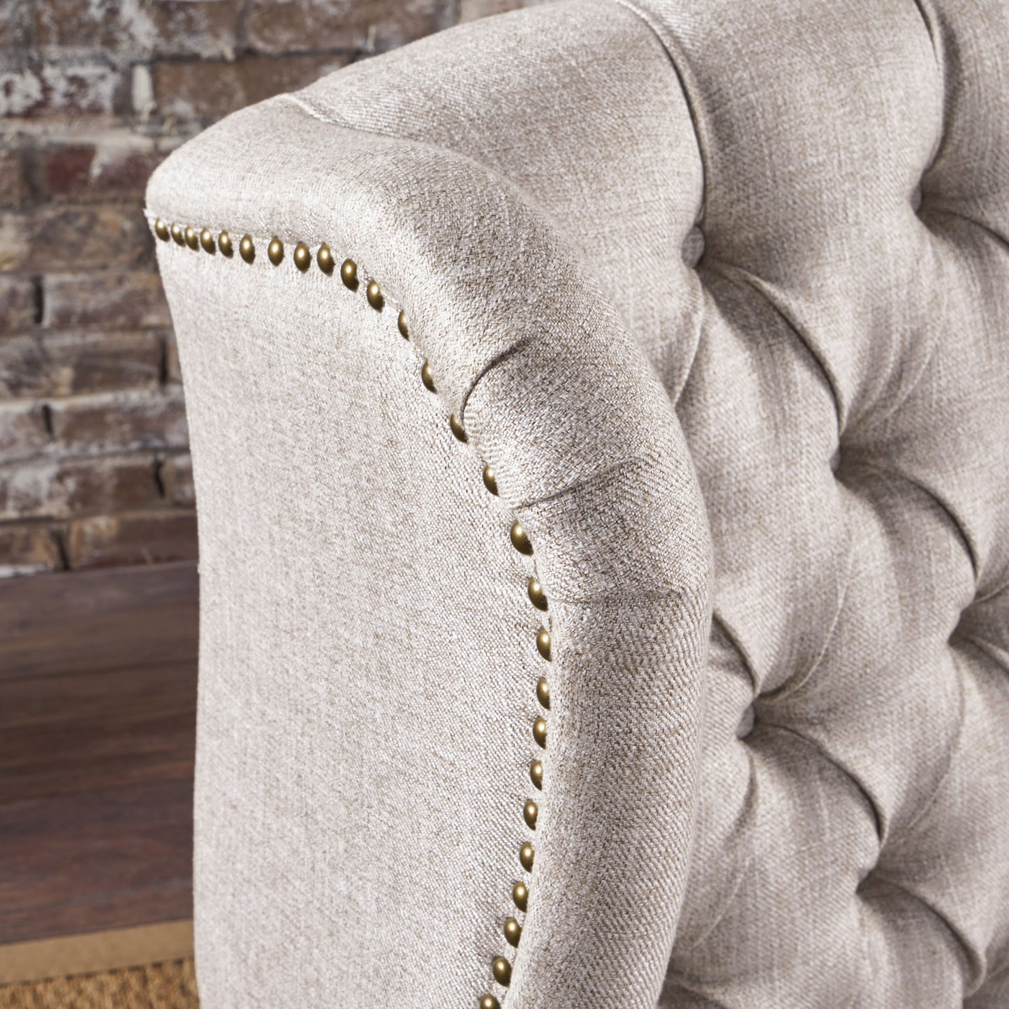 Closeup of a tufted beige linen armchair featuring brass nailhead trim