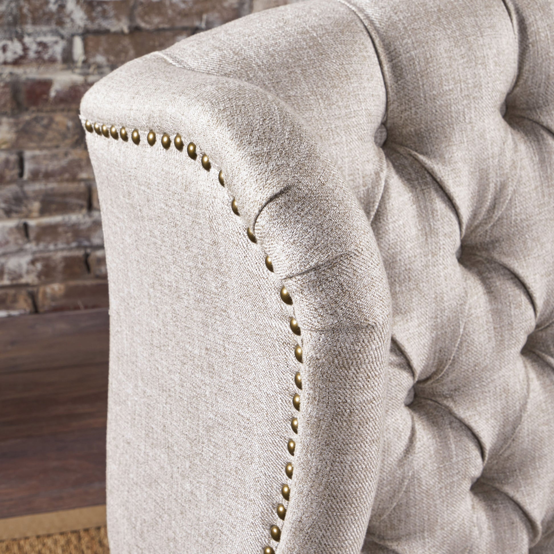 Closeup of a tufted beige linen armchair featuring brass nailhead trim