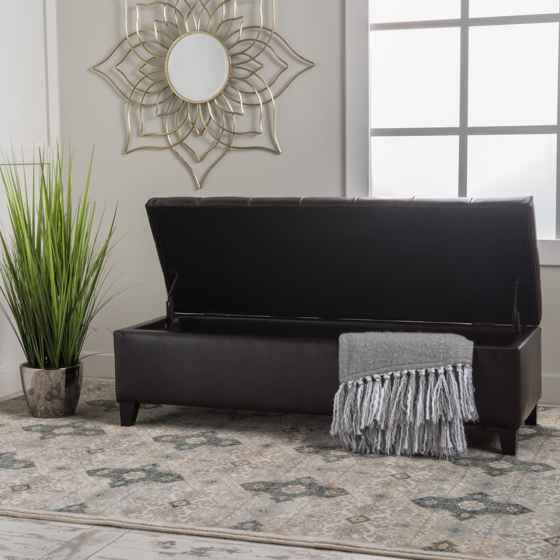 Dark brown faux leather storage ottoman with tufted lid and fringe throw