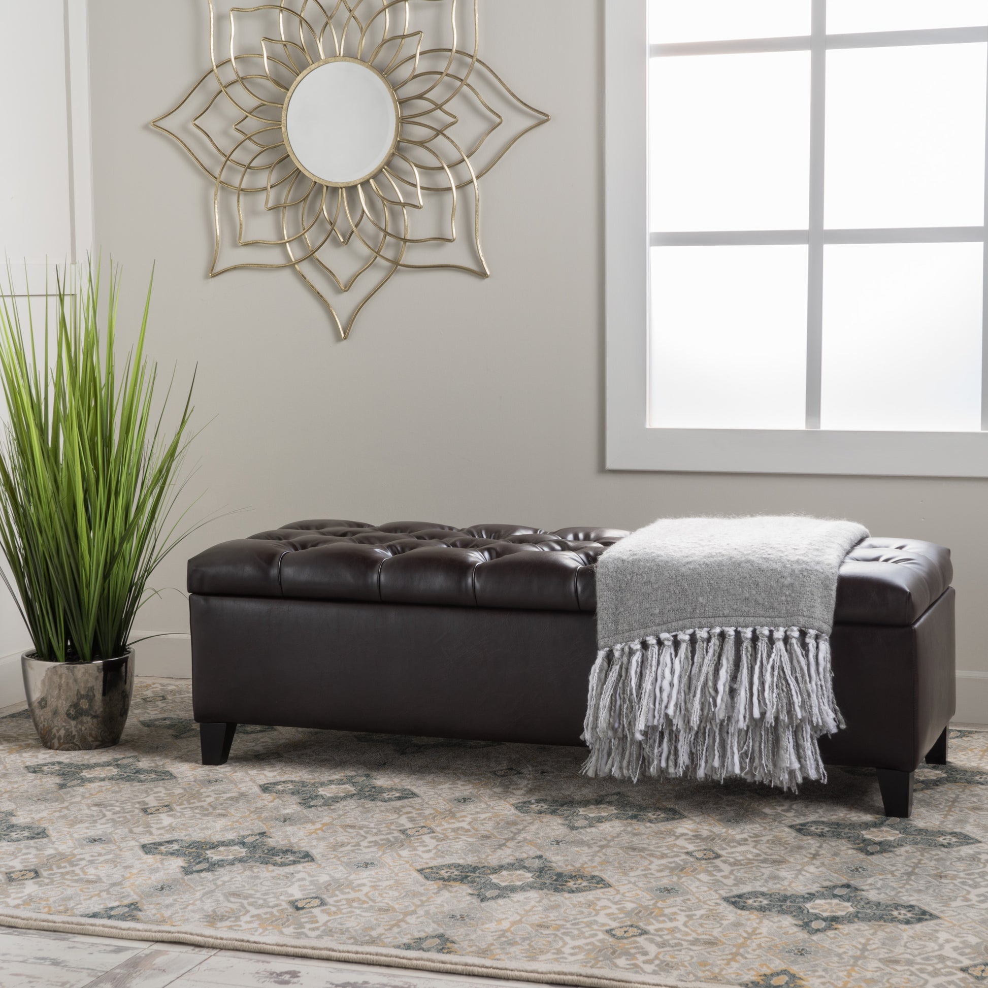 Dark brown tufted faux leather storage ottoman with a grey fringed throw draped over it