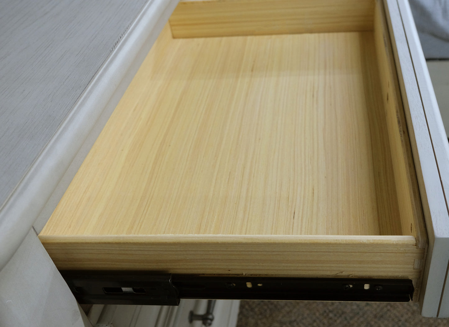 Open light grey dresser drawer with unfinished wood interior and metal glides