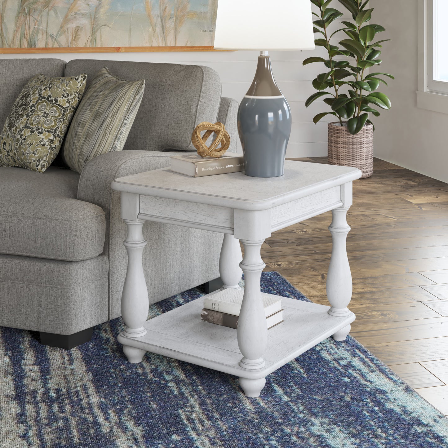 White distressed end table with carved legs and two shelves next to a sofa