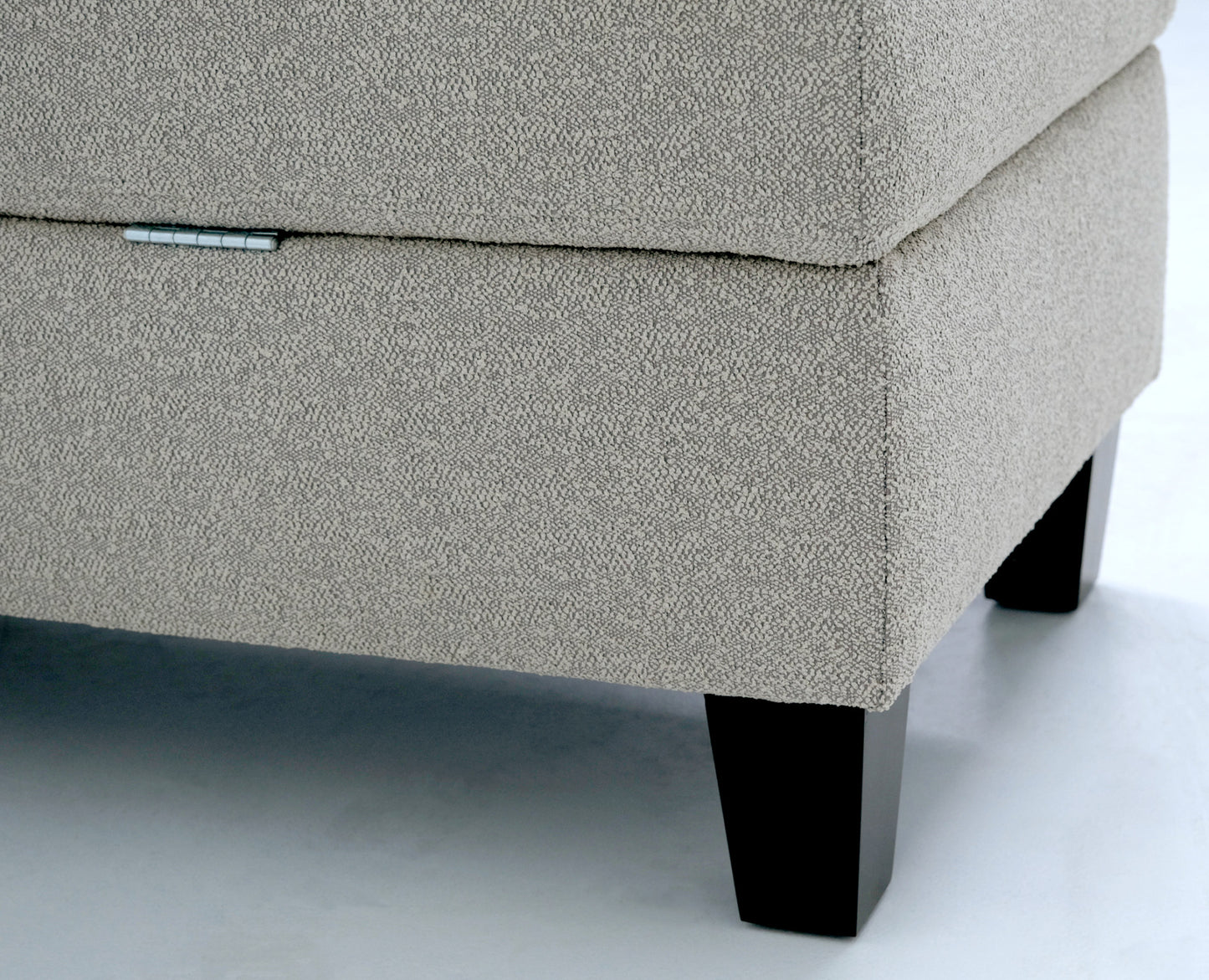 Beige textured fabric storage ottoman with a silver hinge detail and dark wooden legs