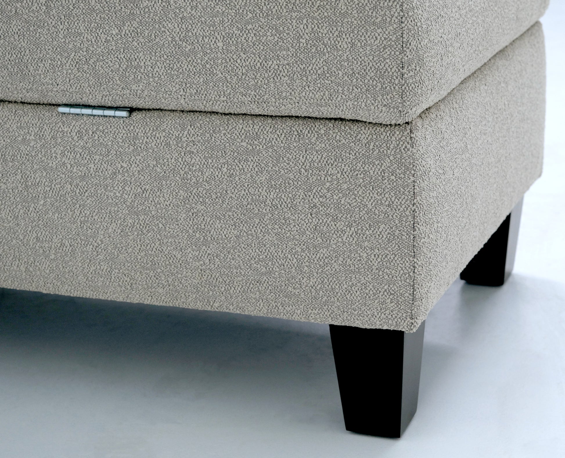 Beige textured fabric storage ottoman with a silver hinge detail and dark wooden legs