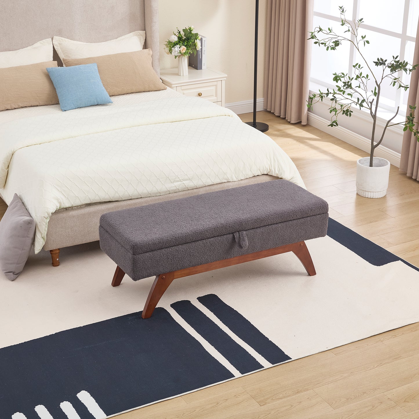 Dark grey fabric storage ottoman with wooden legs at foot of bed