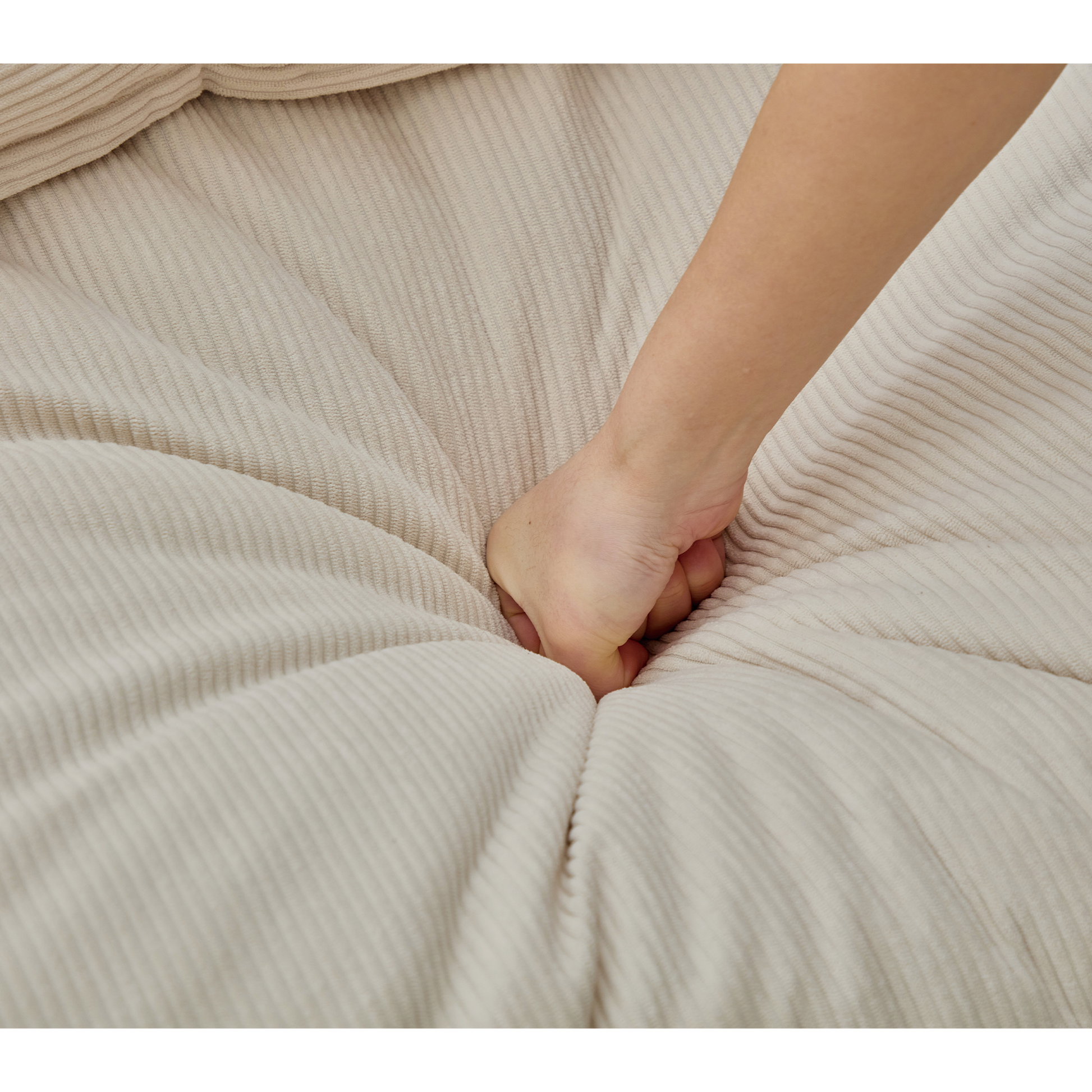 Hand pressing into plush beige corduroy fabric on a comfortable sofa