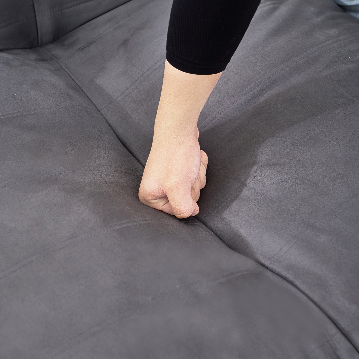 Closeup of hand pressing into a soft charcoal gray microfiber couch cushion