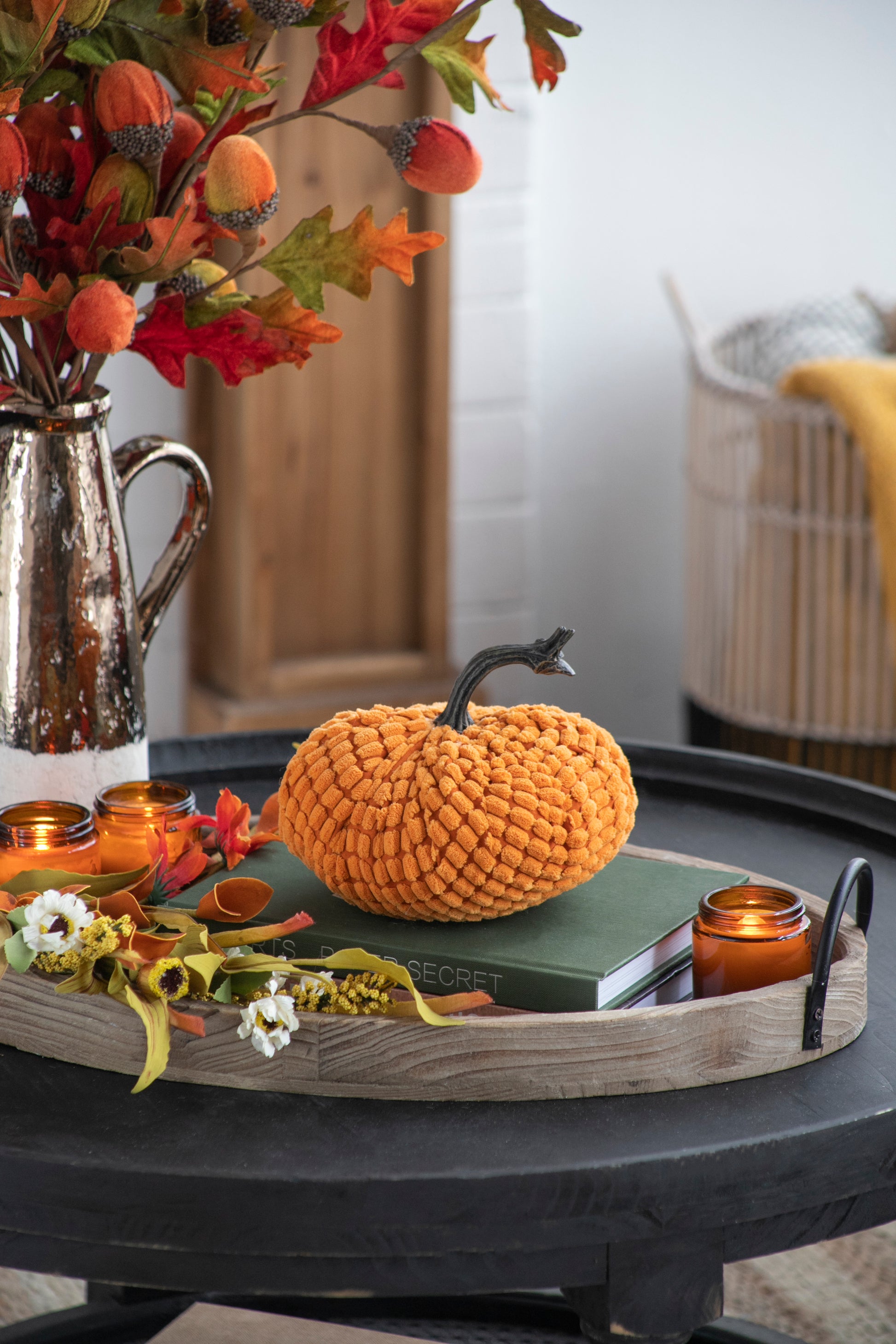Plush orange pumpkin decor with textured finish and dark stem on a rustic wooden tray