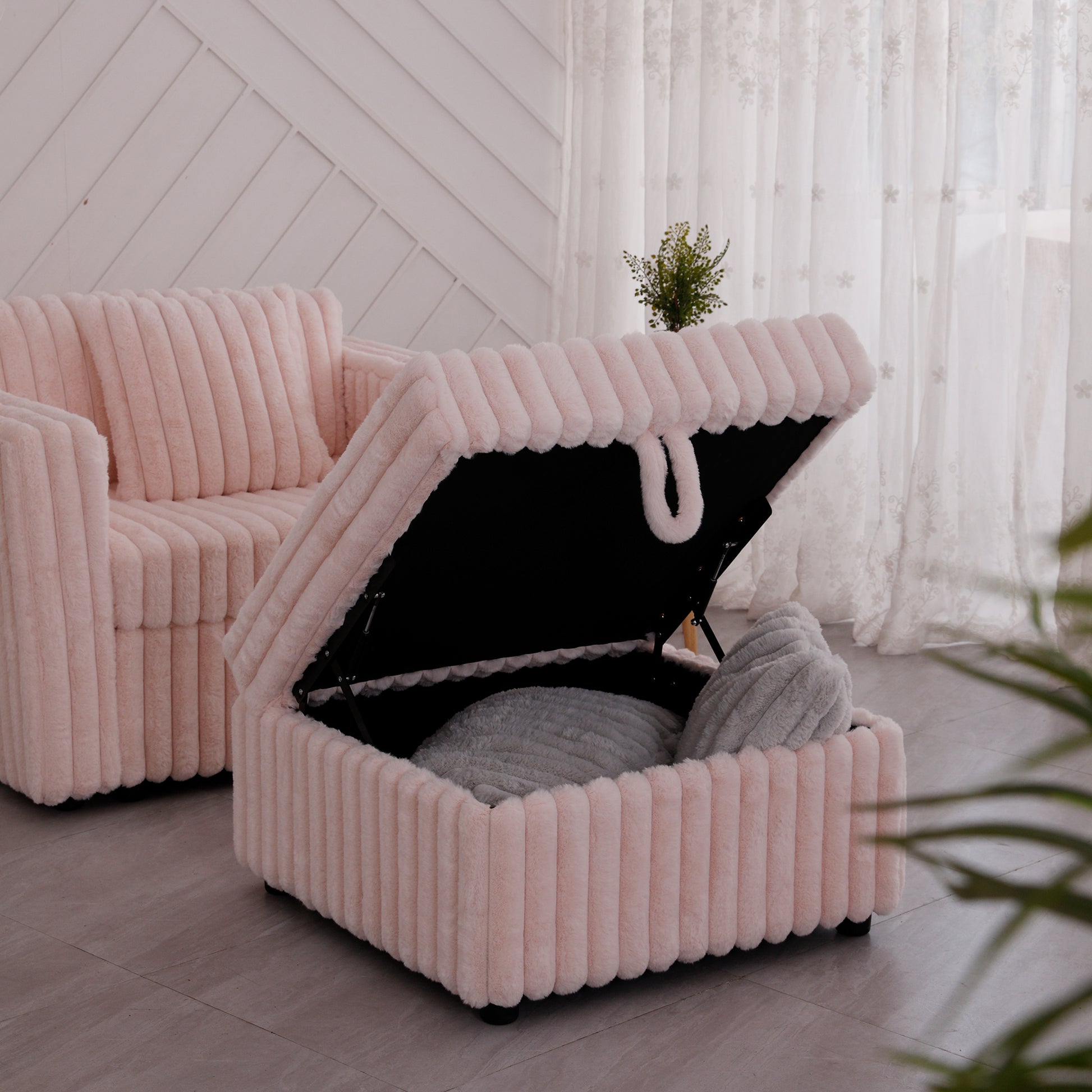 Pink plush ottoman with open lid revealing grey pillows and storage space