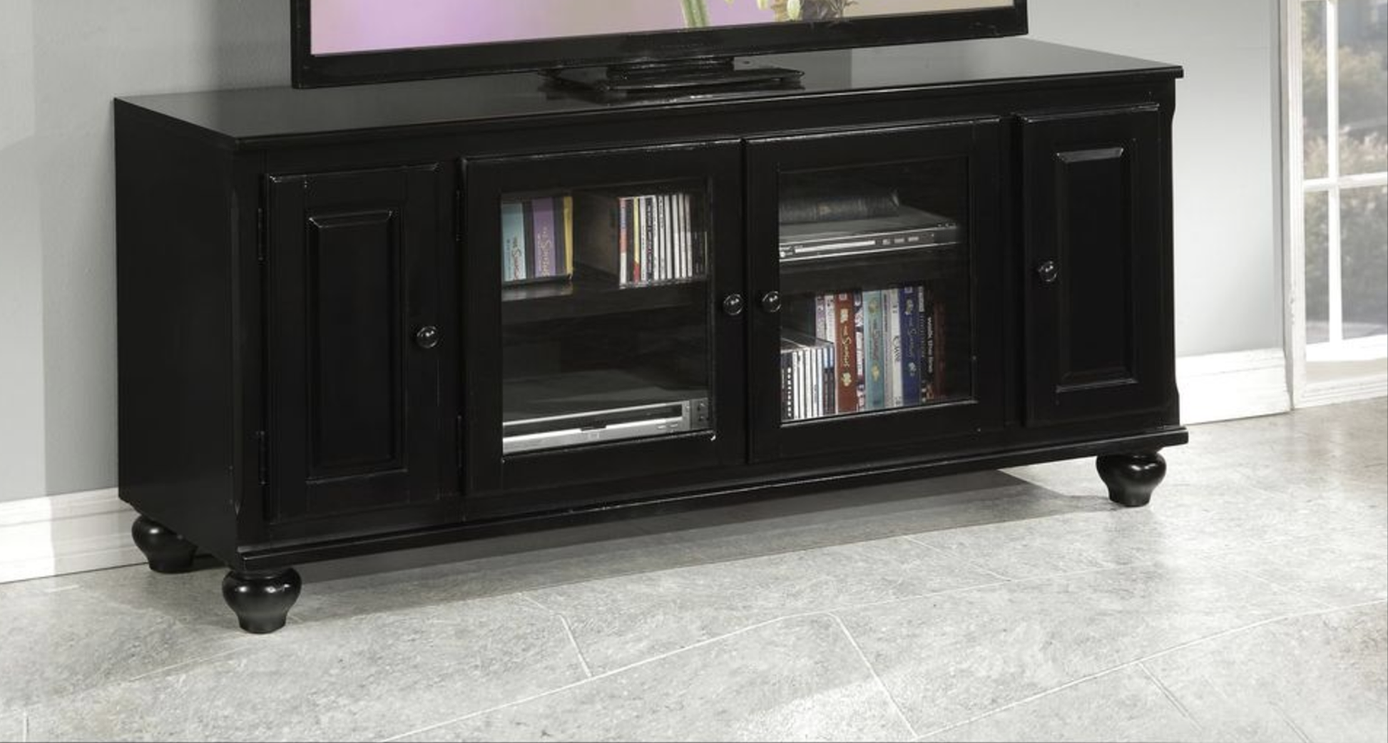 Black wooden media console with glass doors holding DVDs and electronics