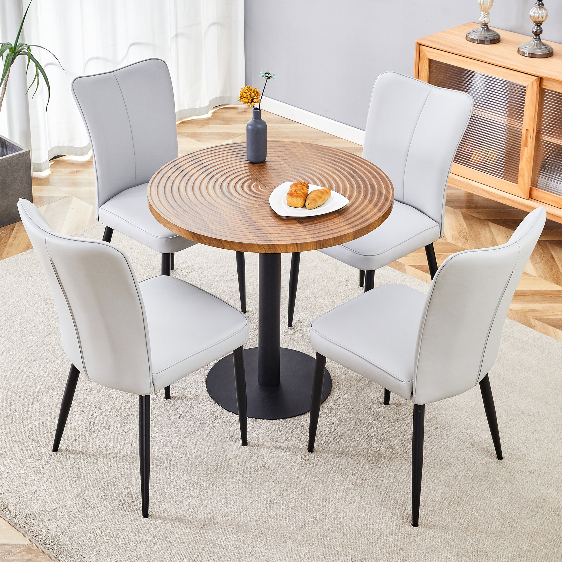 Modern dining set with four light grey faux leather chairs and a round wood table