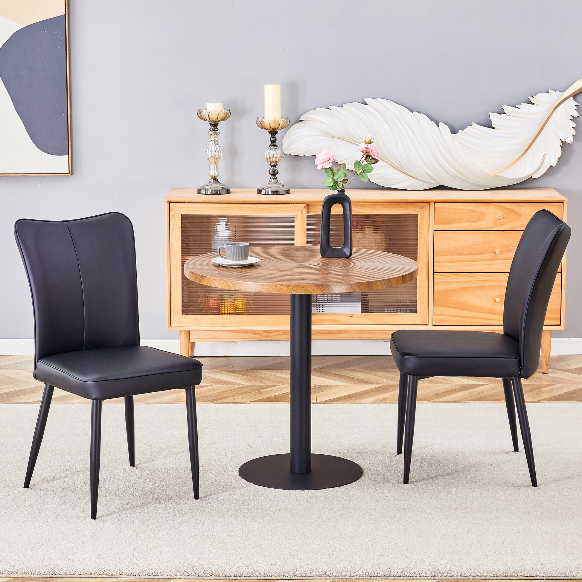 Two black faux leather dining chairs flank a round natural woodgrain table with a black base