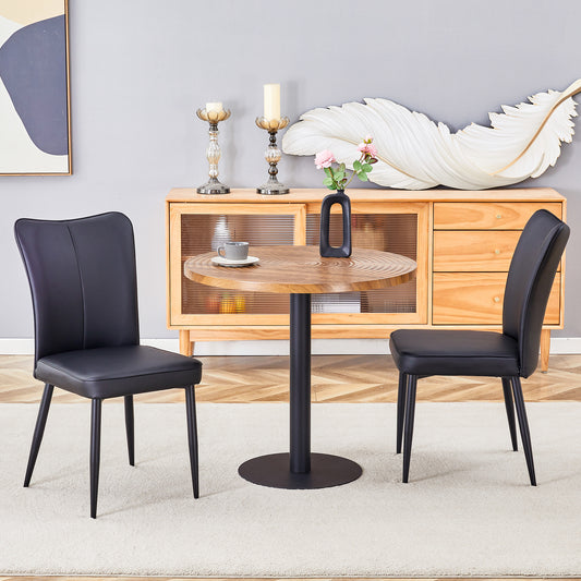 Two black faux leather dining chairs flank a round natural woodgrain table with a black base