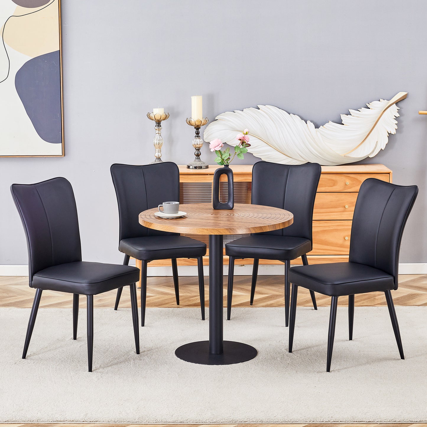 Four black faux leather dining chairs with black metal legs surround a round wood table