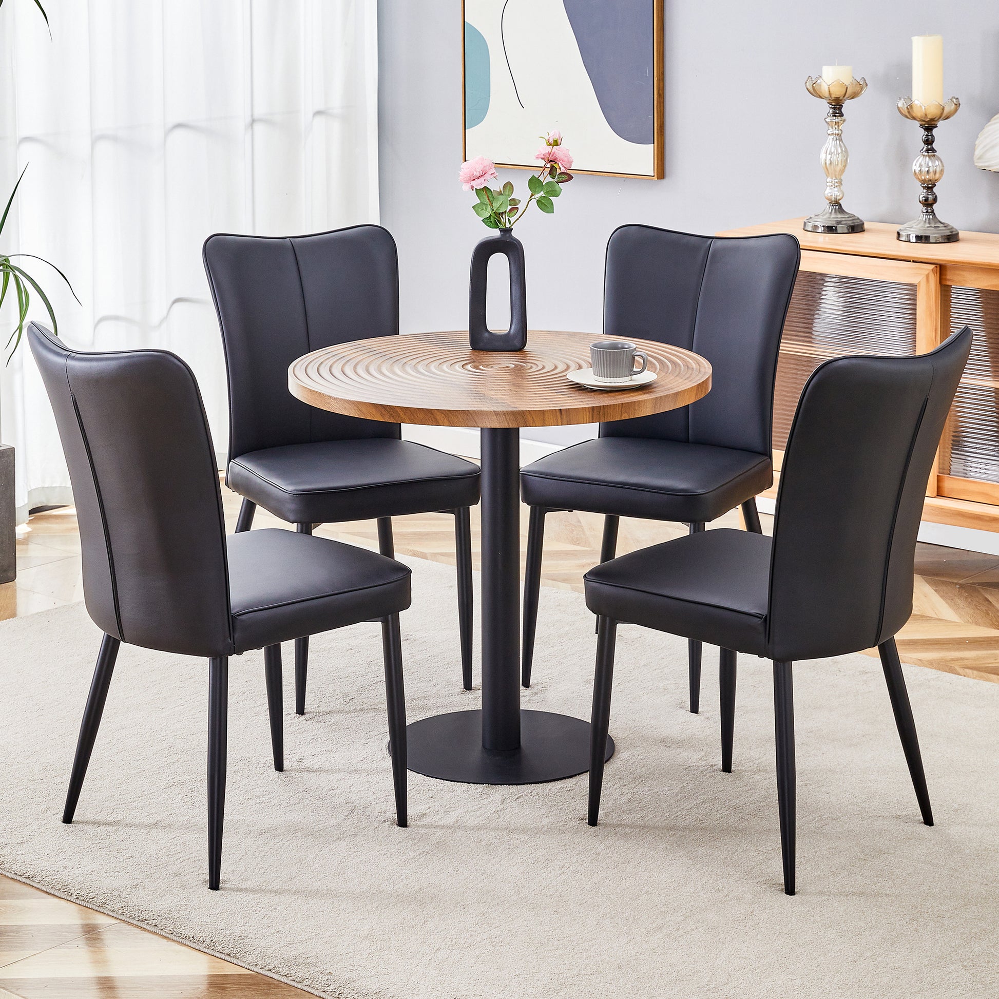 Four black faux leather dining chairs with a contemporary curved back arranged around a round wood table