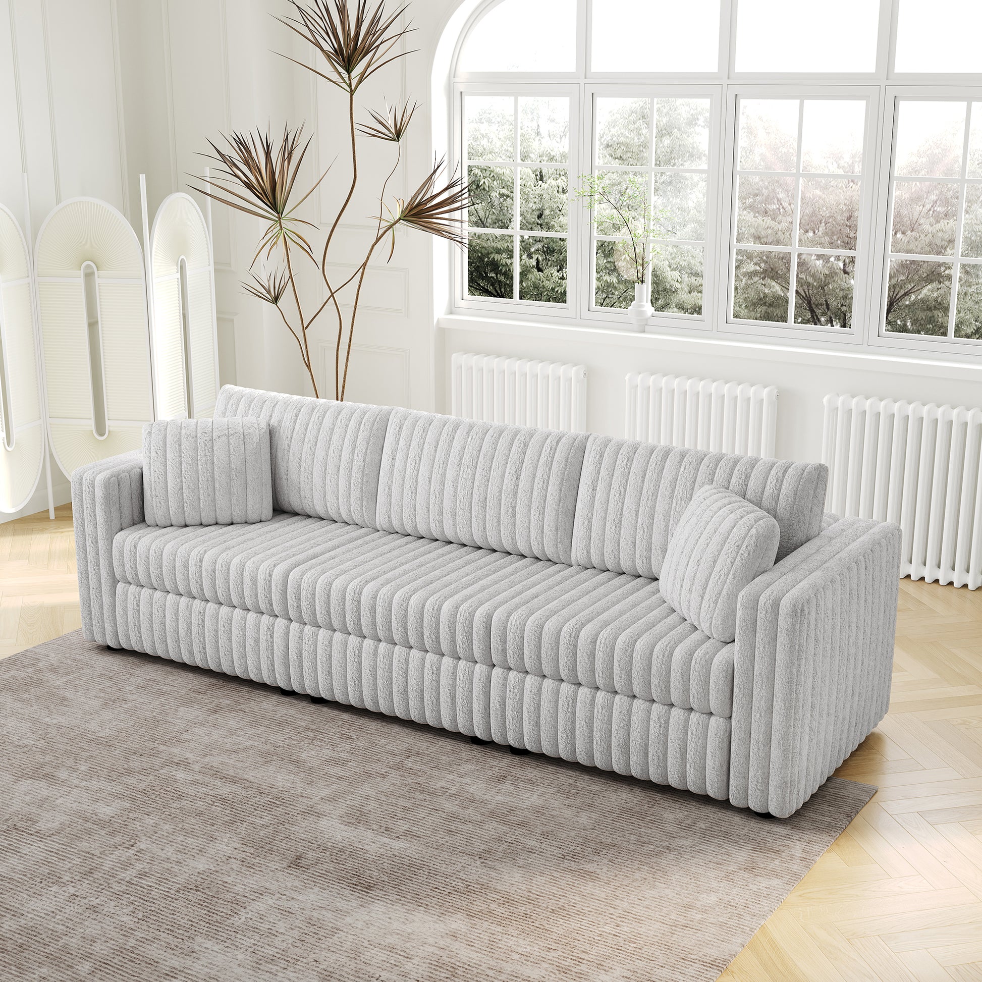 Plush grey upholstered sofa with channel tufting accent pillows and a textured rug