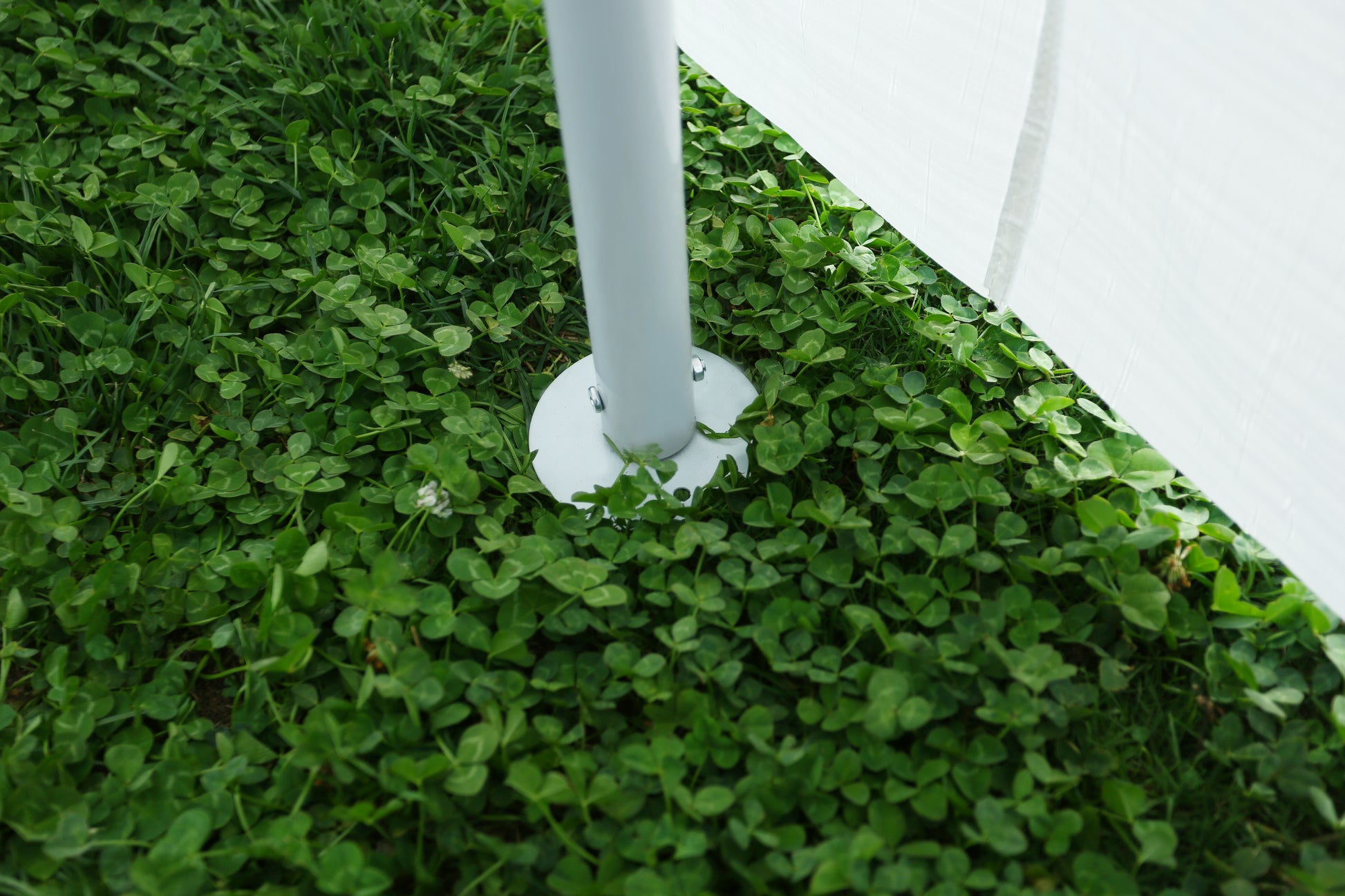 White metal pole with base anchoring a tent in lush green clover lawn