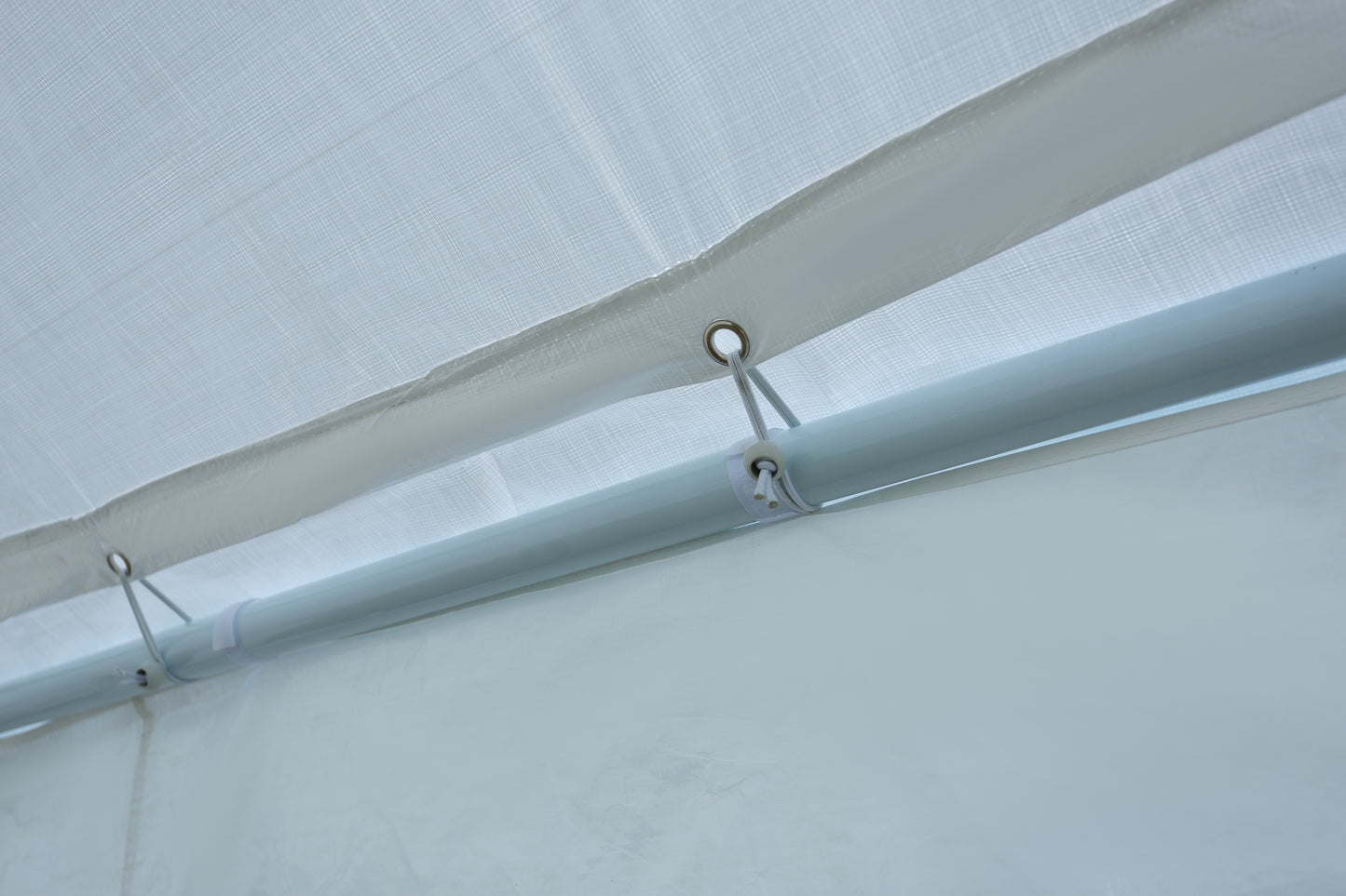 Close up of white polyethylene tarp with reinforced grommets and elastic cords securing it to a metal pole