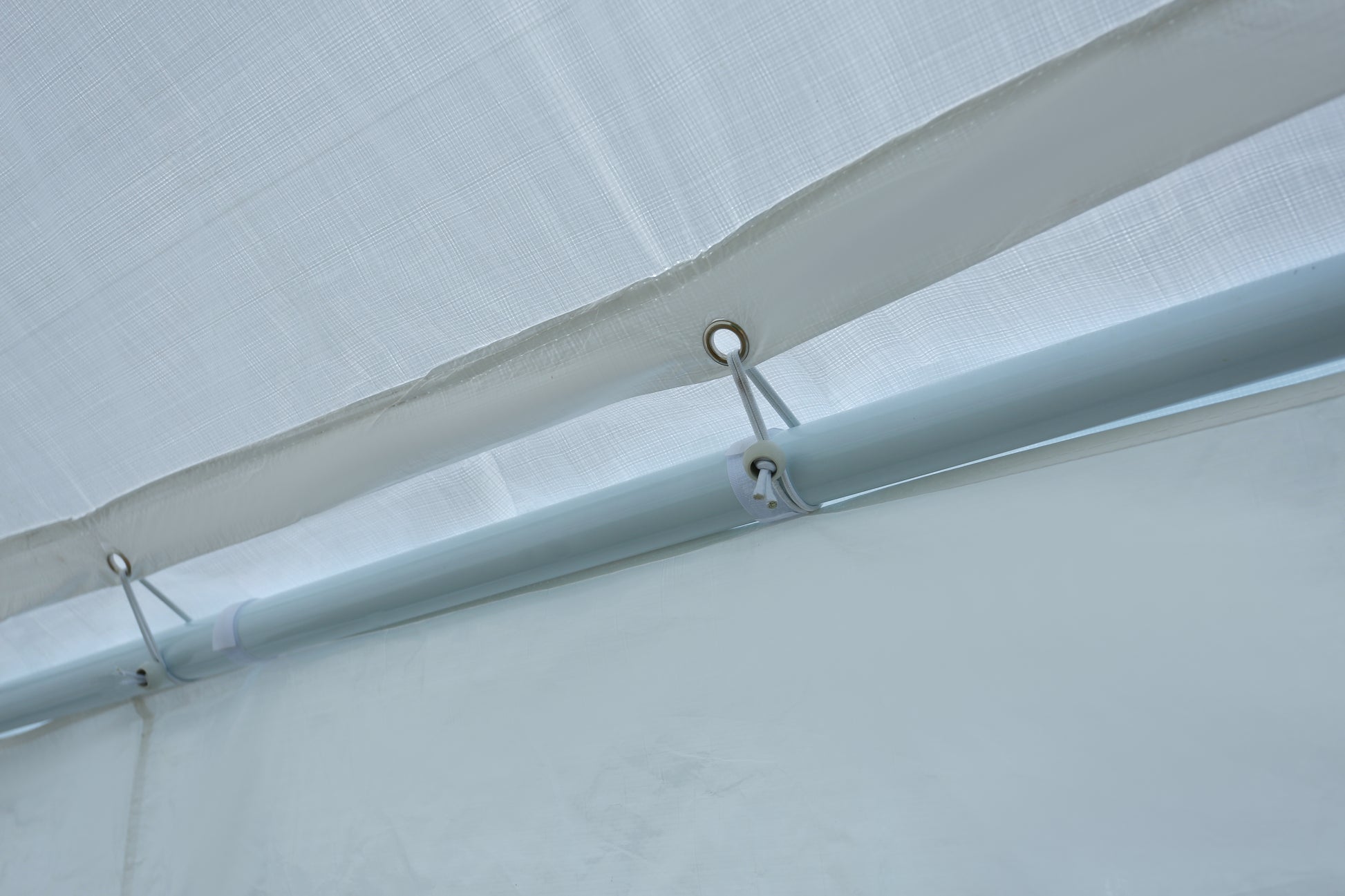 Close up of white polyethylene tarp with reinforced grommets and elastic cords securing it to a metal pole