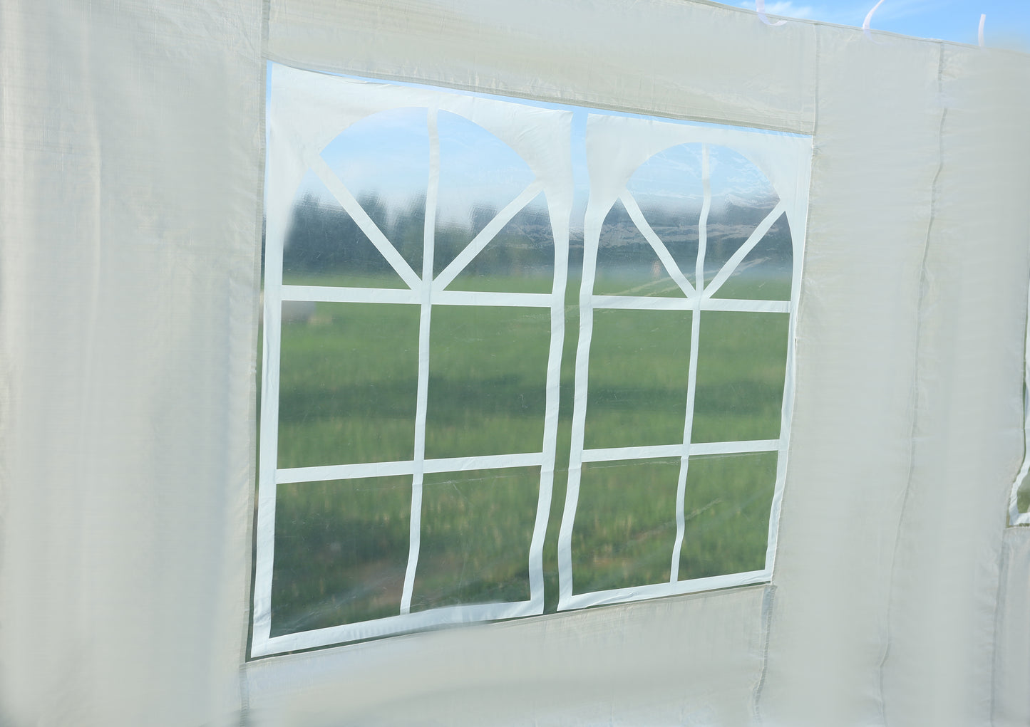 White tent window with clear pane and white cross detailing reflecting outdoor greenery