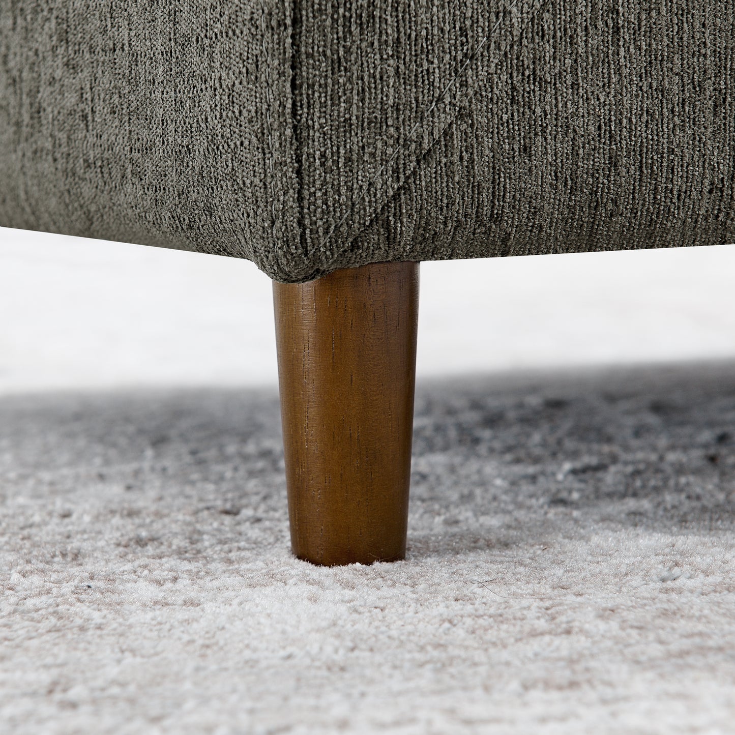 Closeup of a dark grey textured fabric sofa leg with a tapered wooden support