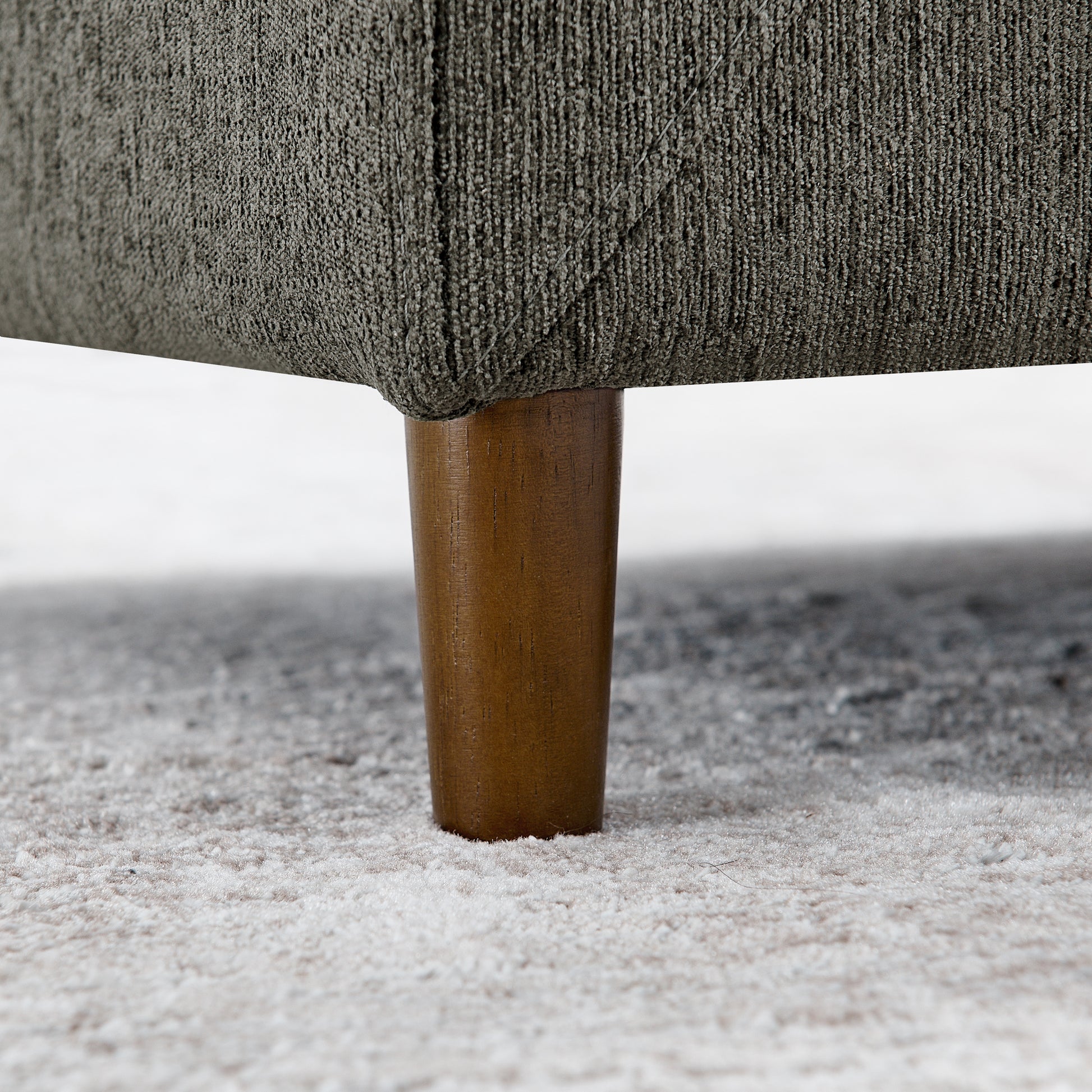 Closeup of a dark grey textured fabric sofa leg with a tapered wooden support