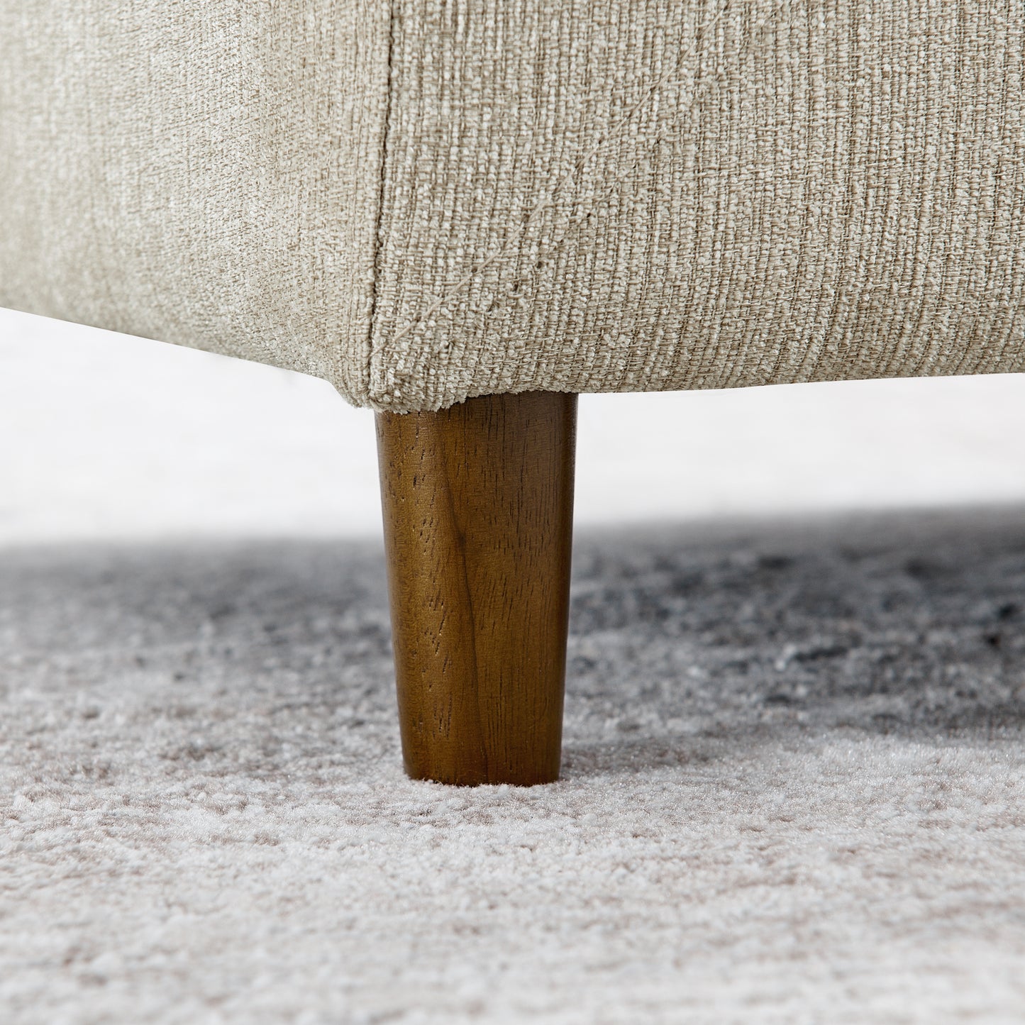 Closeup of a tan textured fabric sofa leg with a rich wood finish