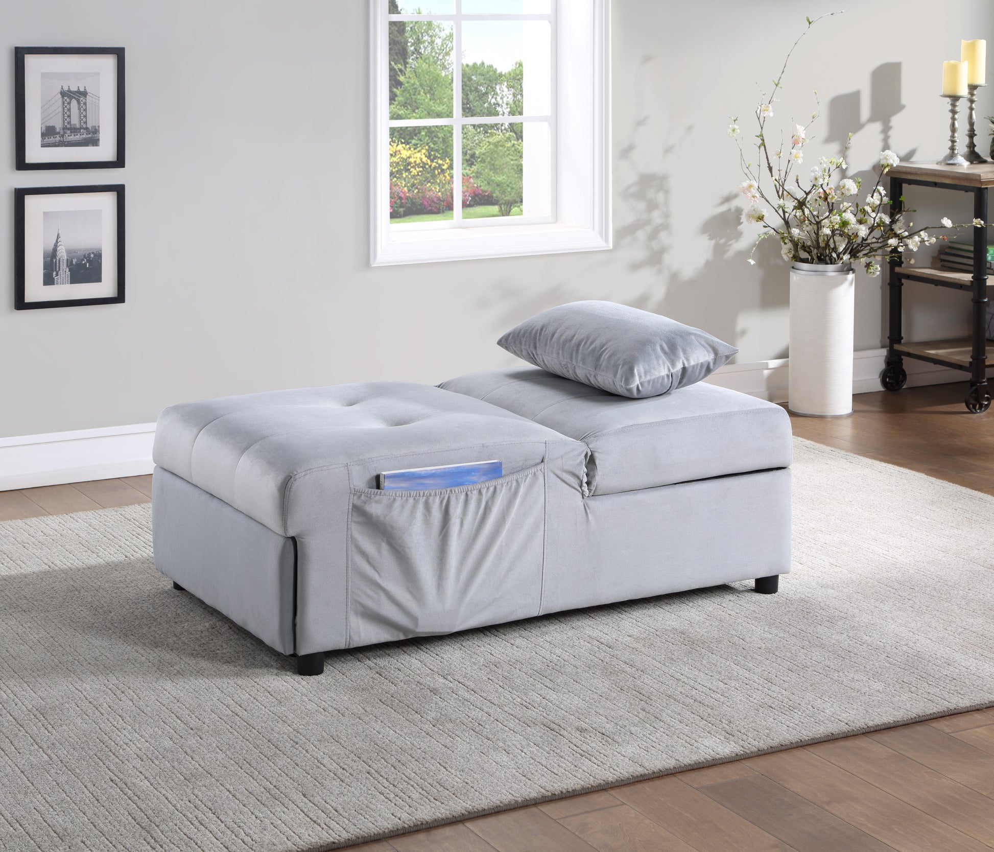 Light gray upholstered ottoman with tufted top and side pocket holding a book
