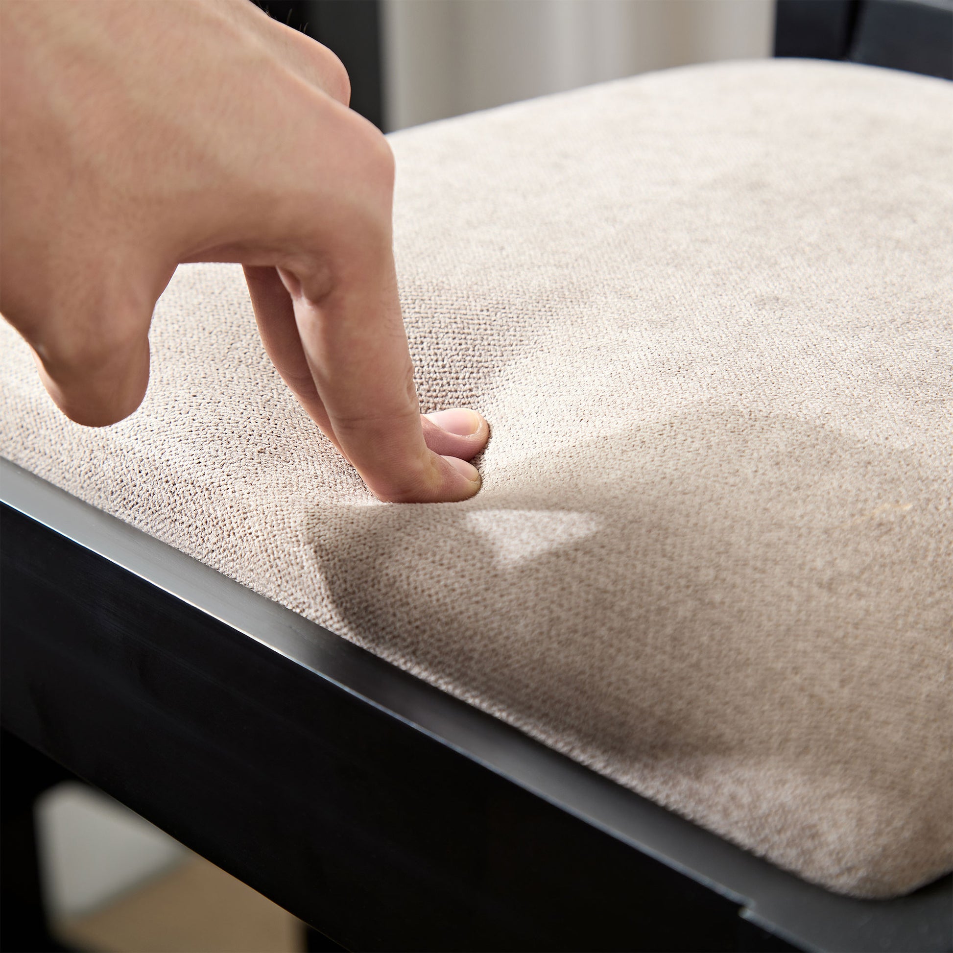 Closeup of a finger pressing into a beige upholstered dining chair cushion for comfort