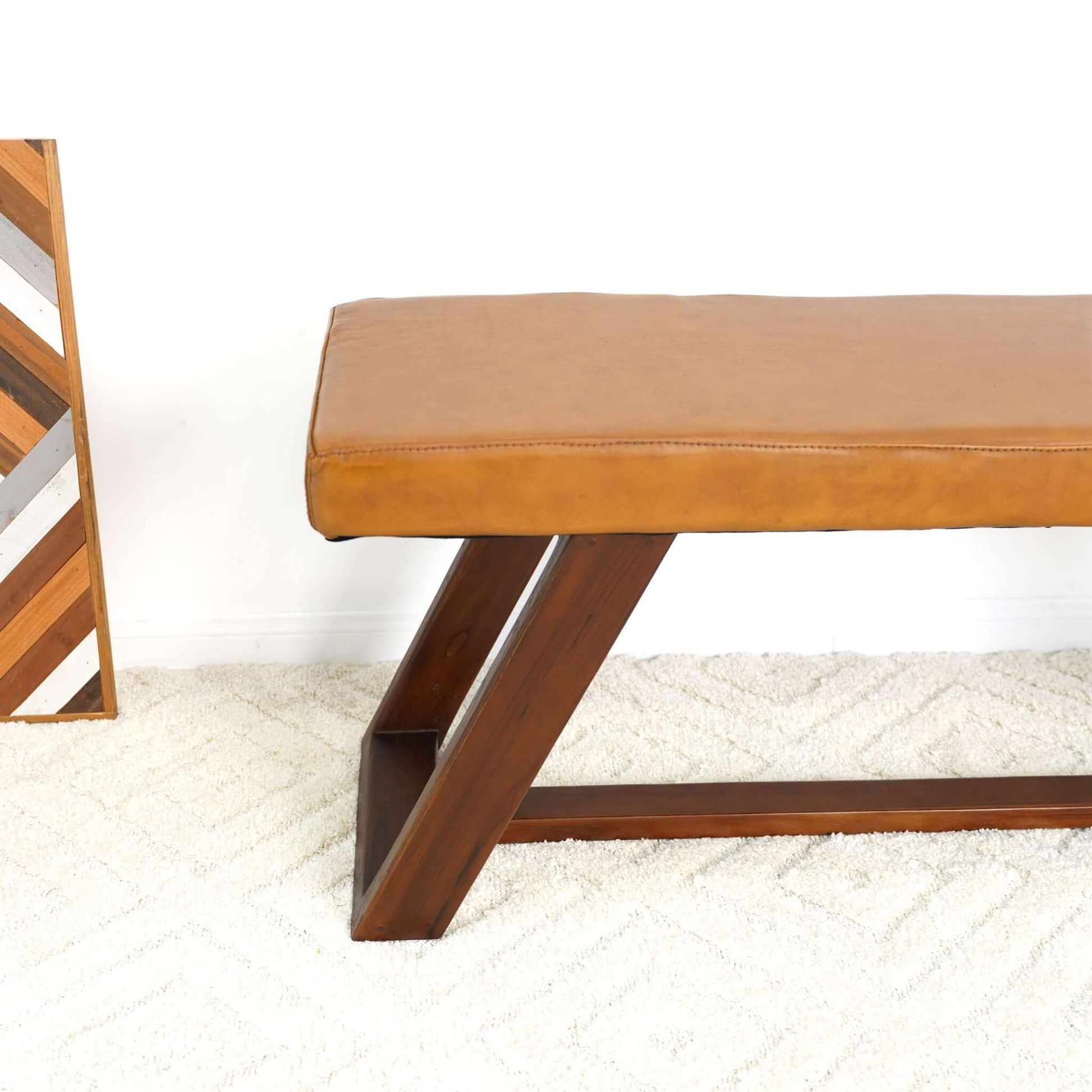 Tan leather bench with dark wood geometric base on a fluffy white rug