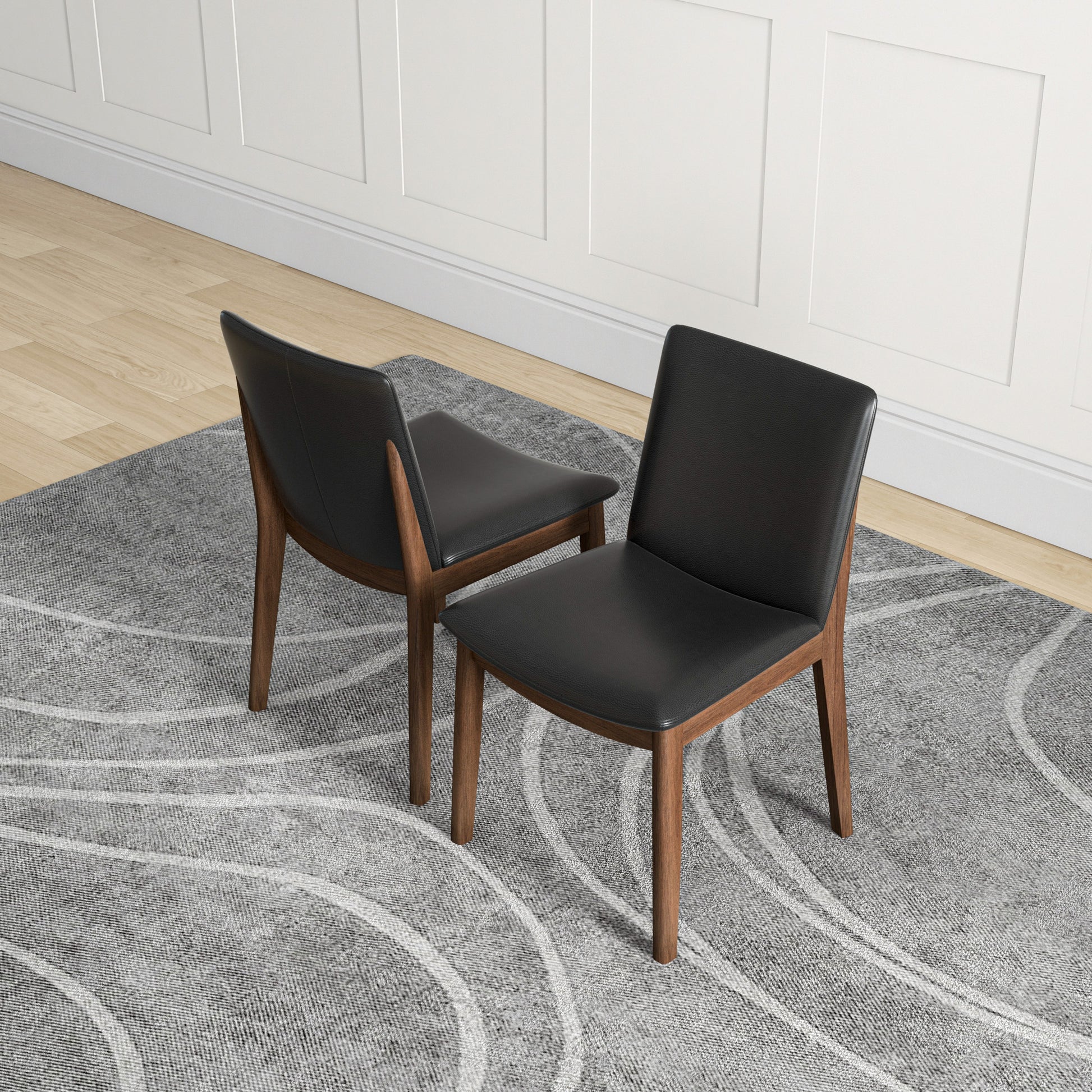 Two black leather dining chairs with walnut frames on a grey patterned rug