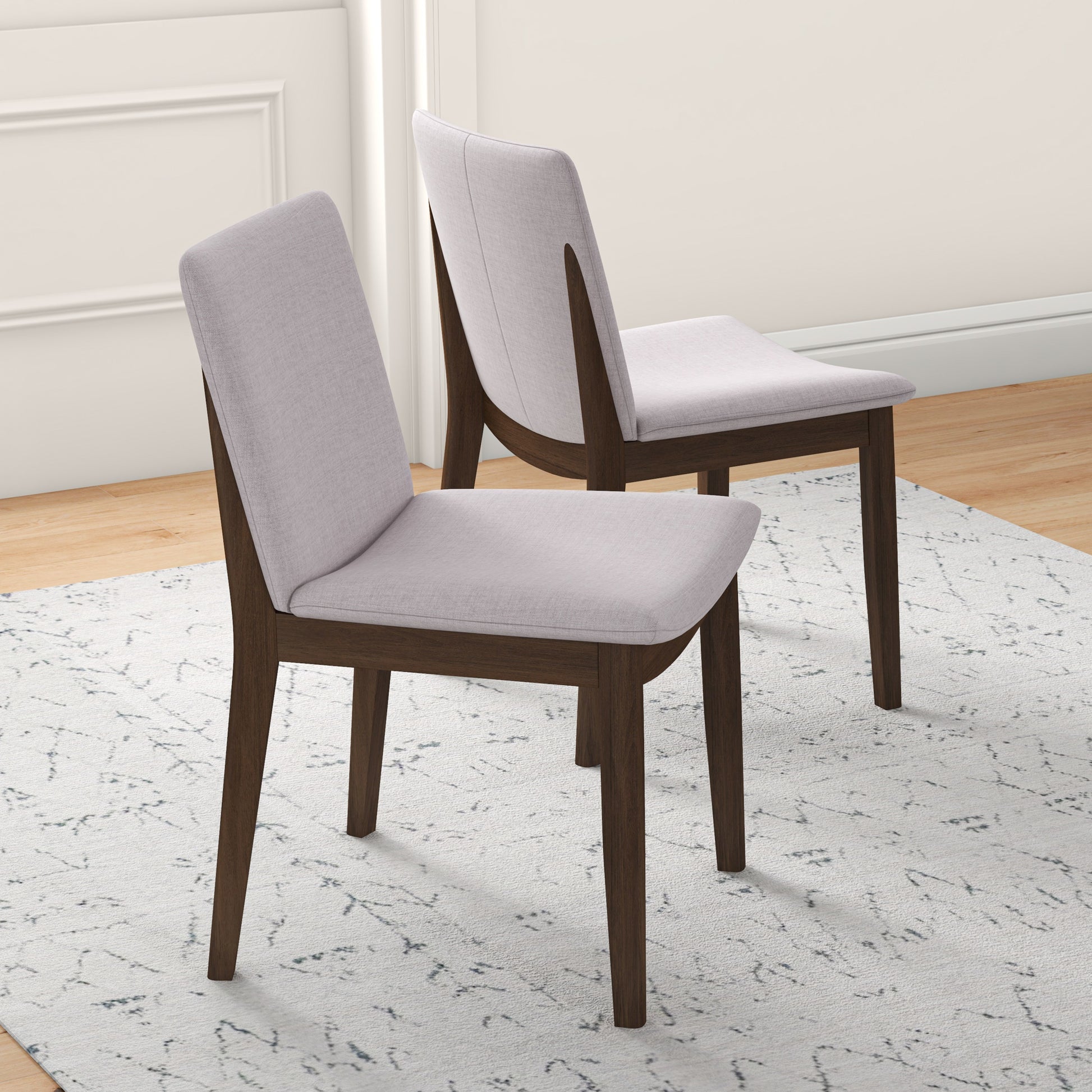 Two upholstered dining chairs with light grey fabric seats and dark wood legs on a patterned rug