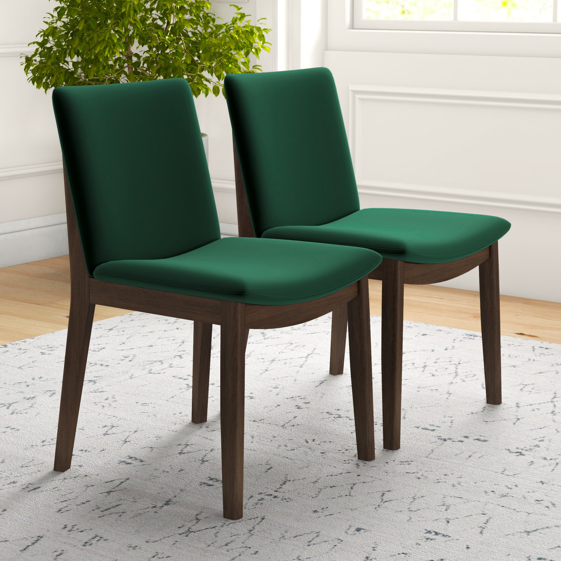 Two emerald green velvet dining chairs with dark wood frames on a textured rug