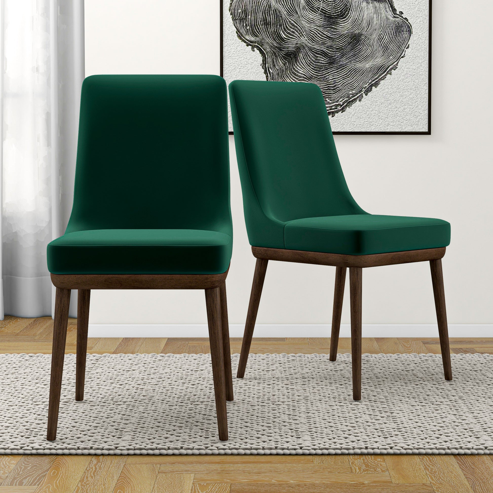 Two plush emerald green velvet dining chairs with dark wood legs on a rug