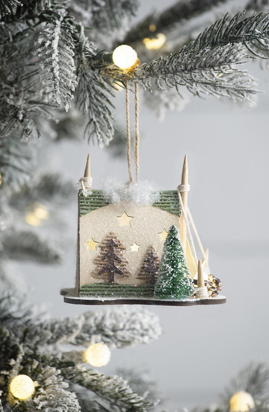 Whimsical Christmas ornament depicting a miniature winter village scene with pine trees and glowing stars