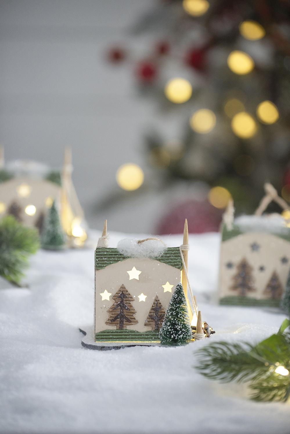 Wooden Christmas house with tree and star cutouts illuminated from within on a snowy surface
