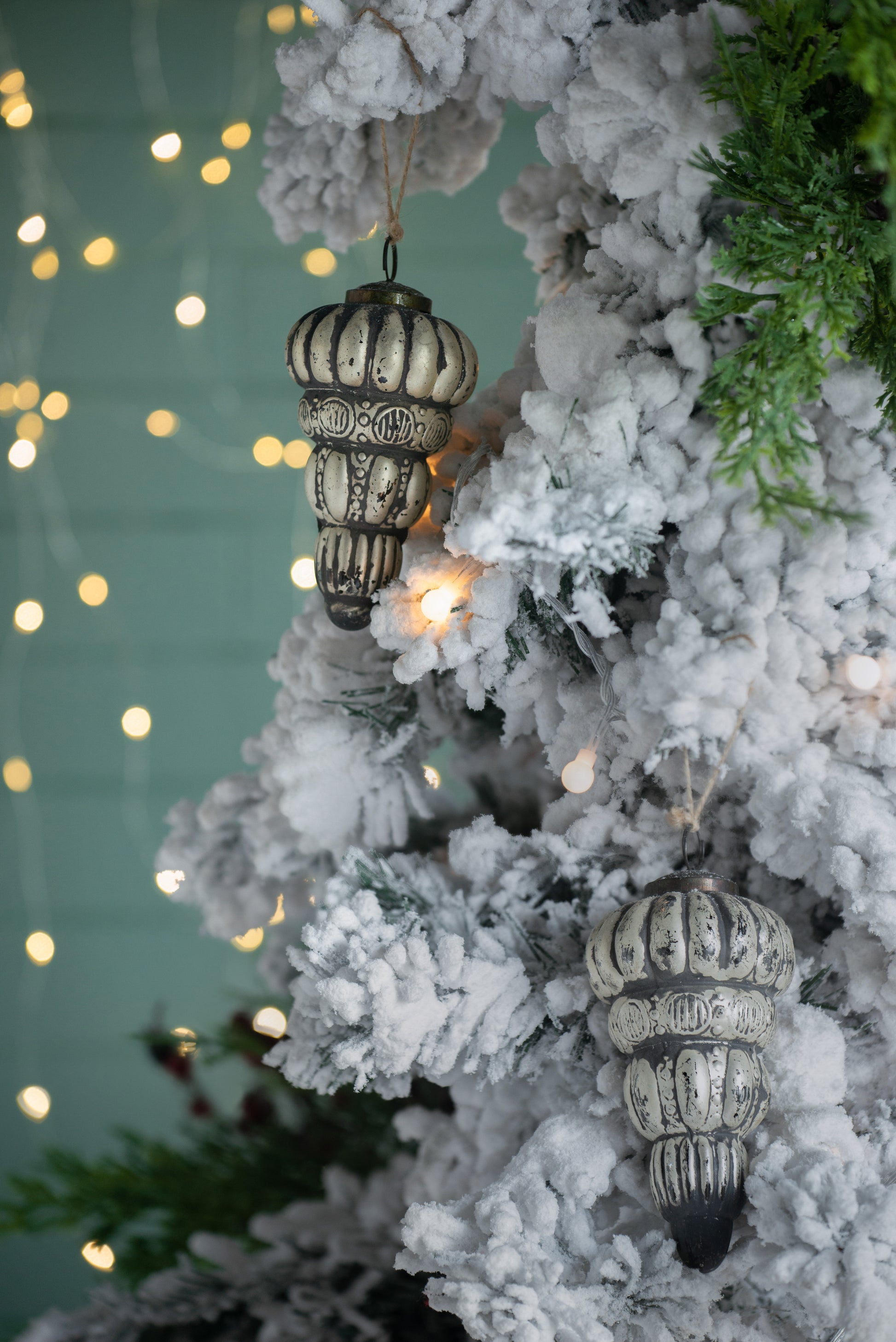 Antique silver Christmas ornament with textured design hanging on snowy tree