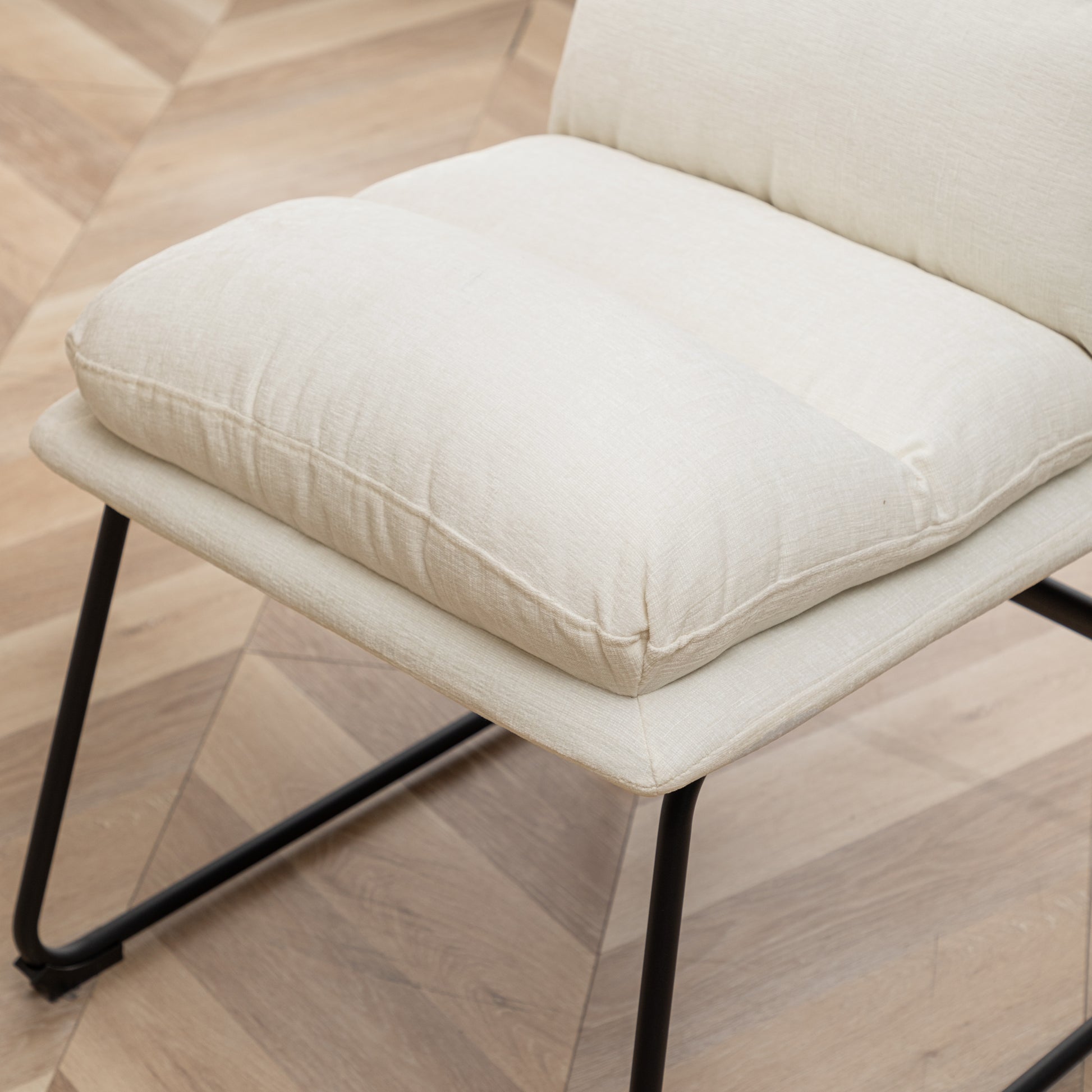 Closeup of a textured cream fabric accent chair with thin black metal legs