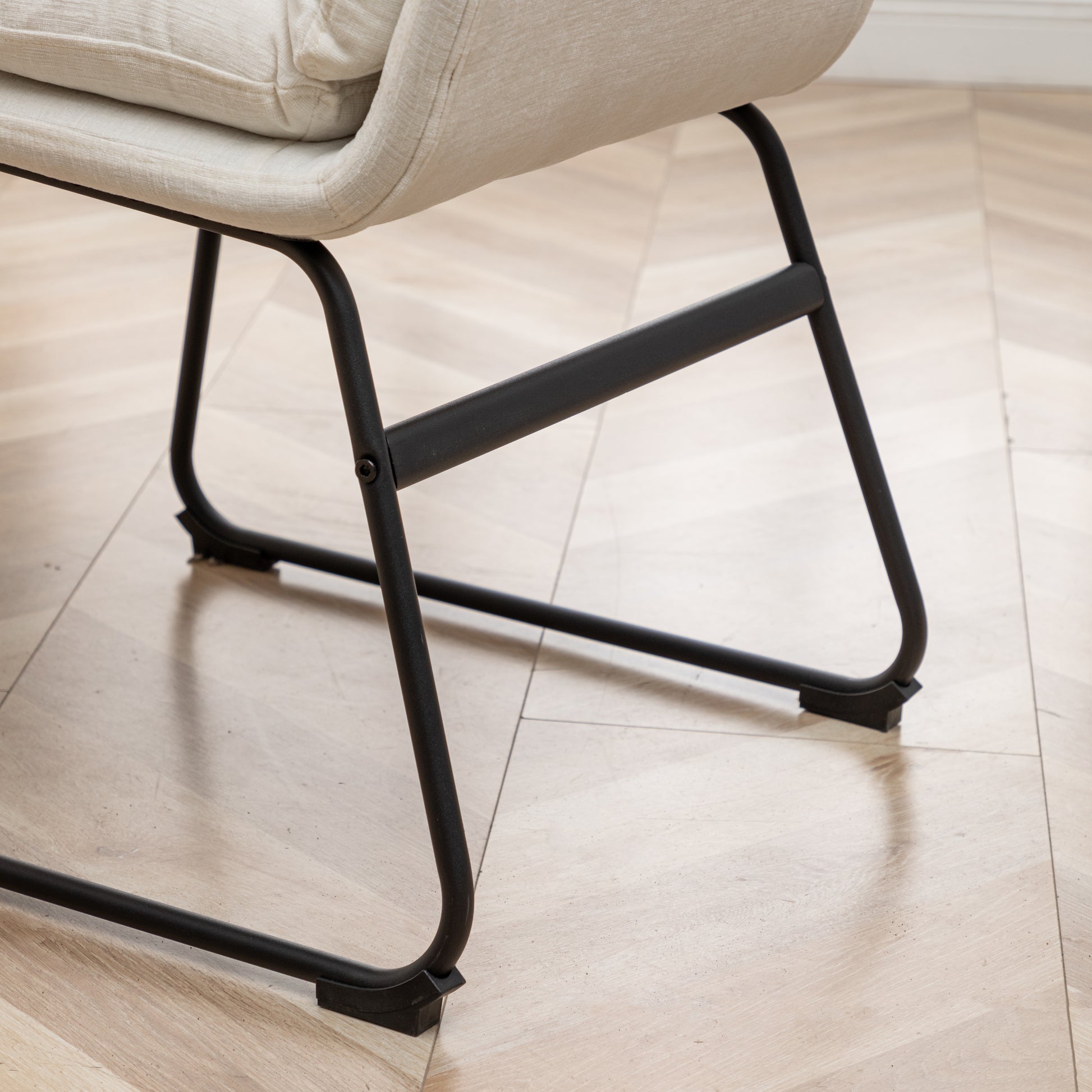 Closeup of a cream textured fabric armchair with black metal legs on a light wood floor