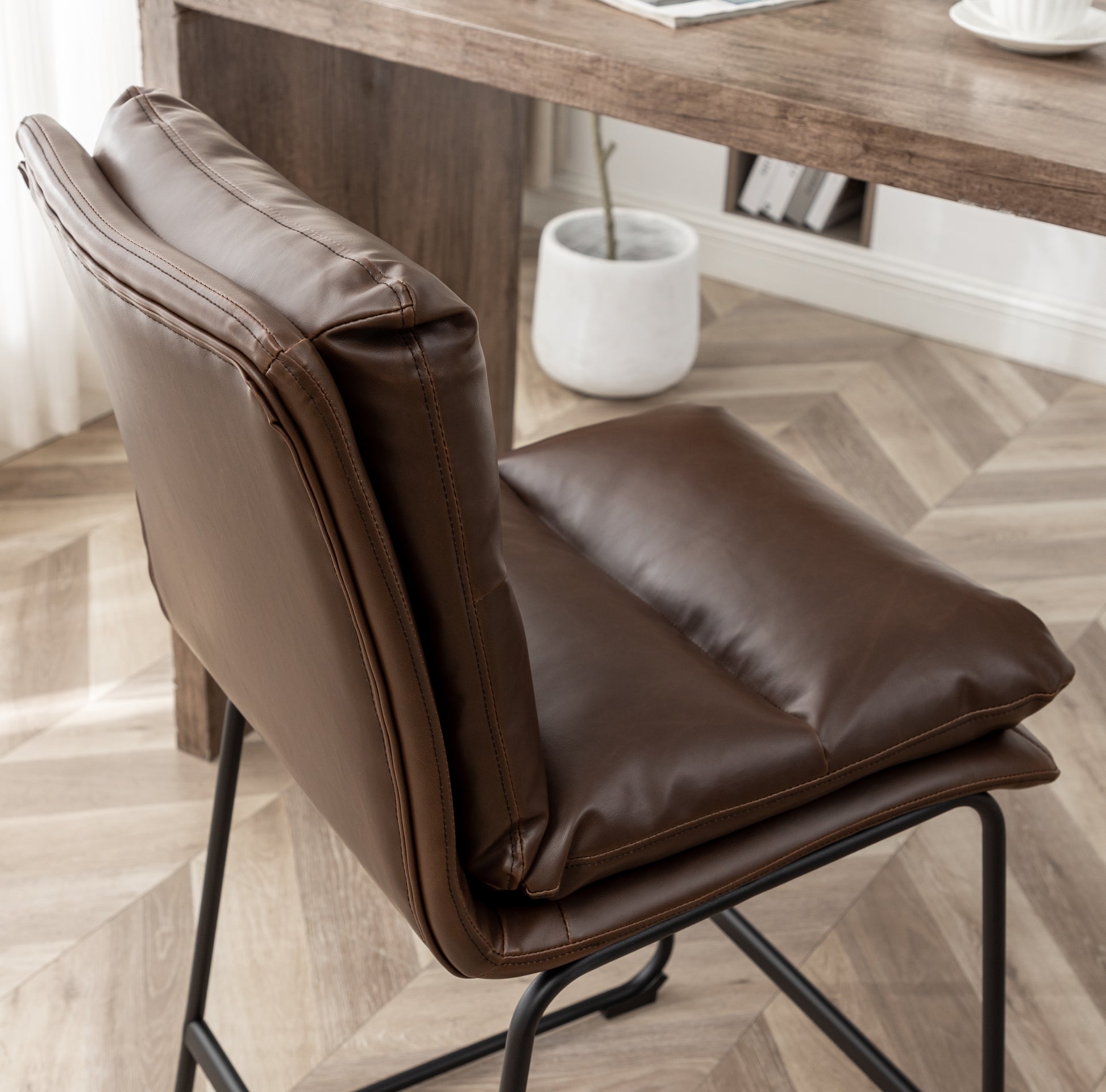 Modern brown faux leather accent chair with stitched details and black metal legs