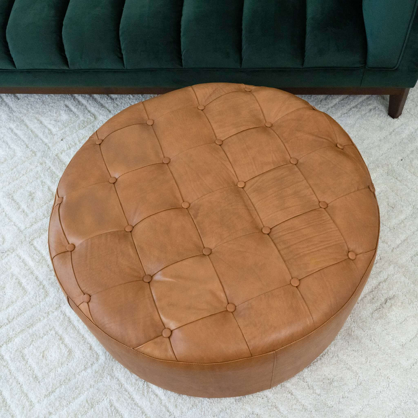 Round cognac leather tufted ottoman with button accents and subtle stitching detail on textured rug