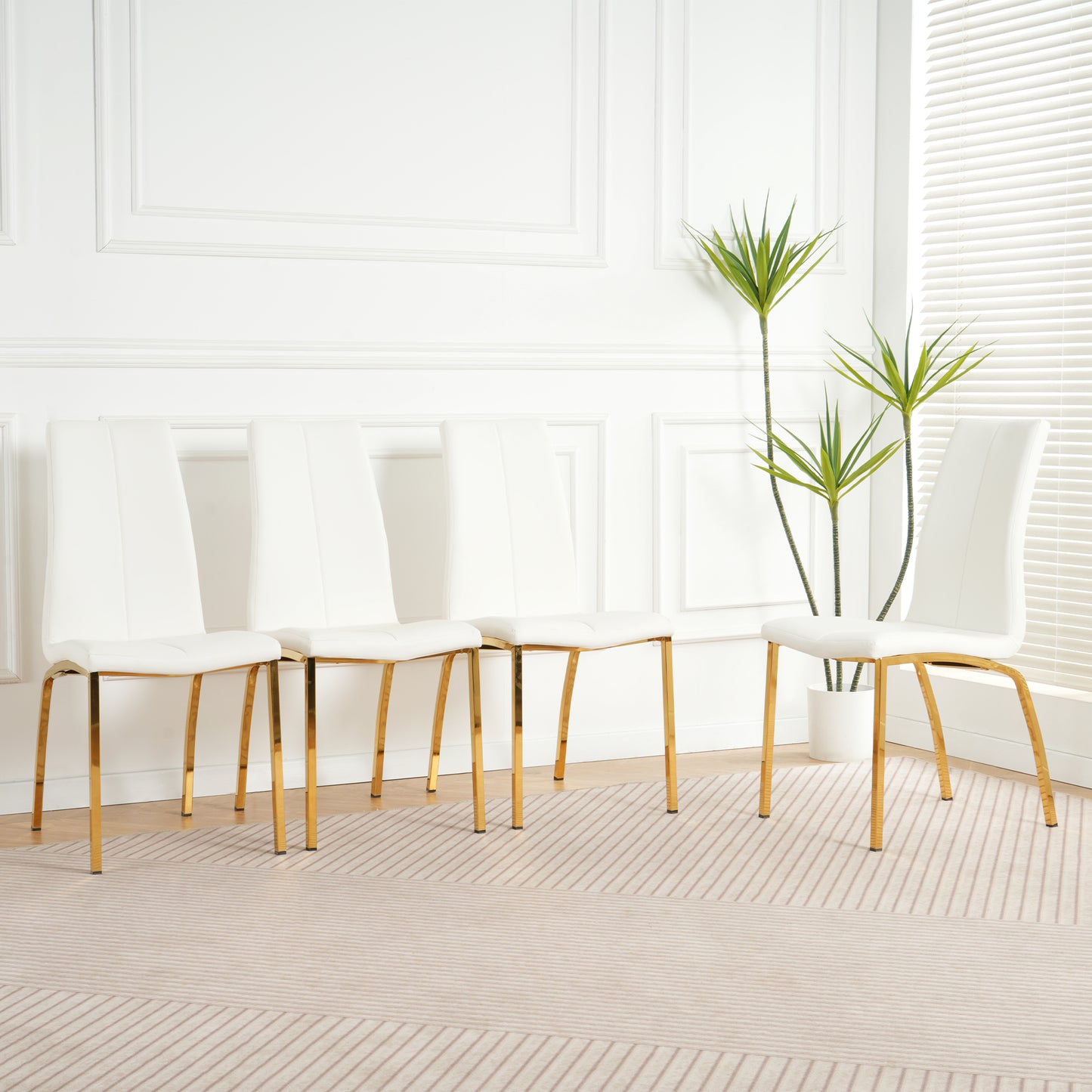 Four white faux leather dining chairs with sleek gold legs in a modern dining room setting