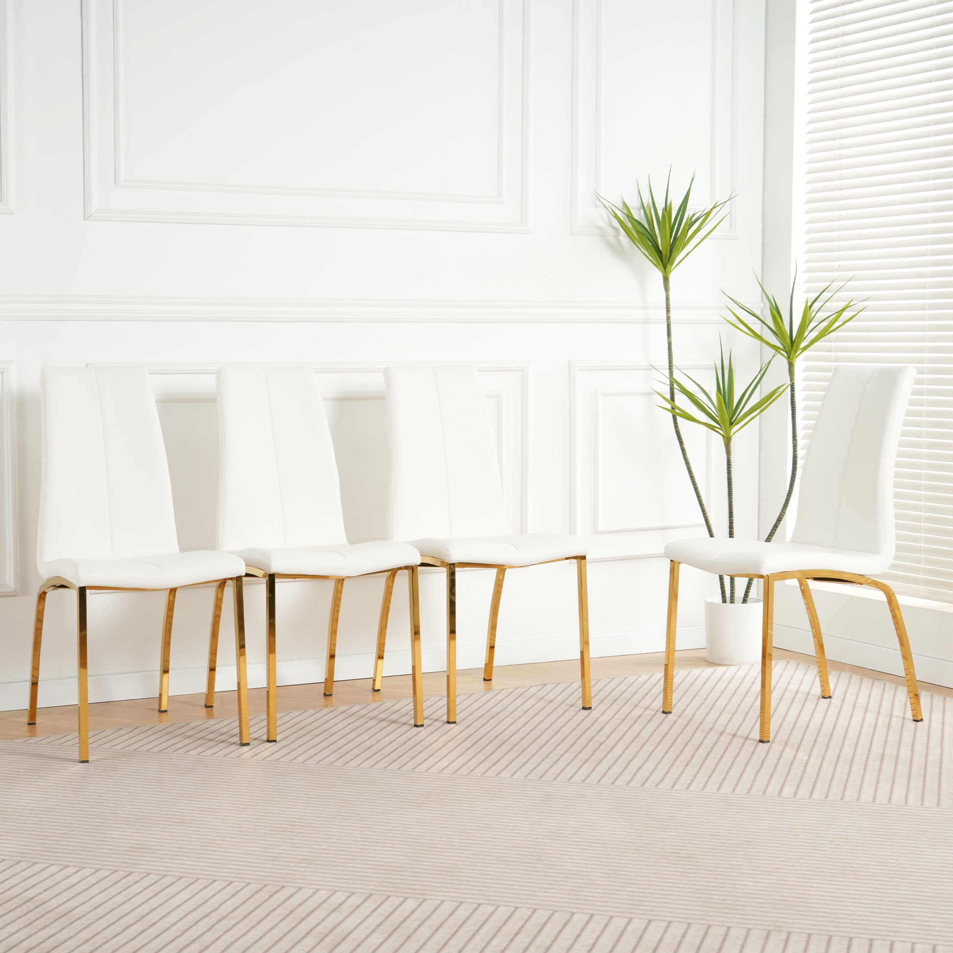 Four white faux leather dining chairs with sleek gold legs in a modern dining room setting