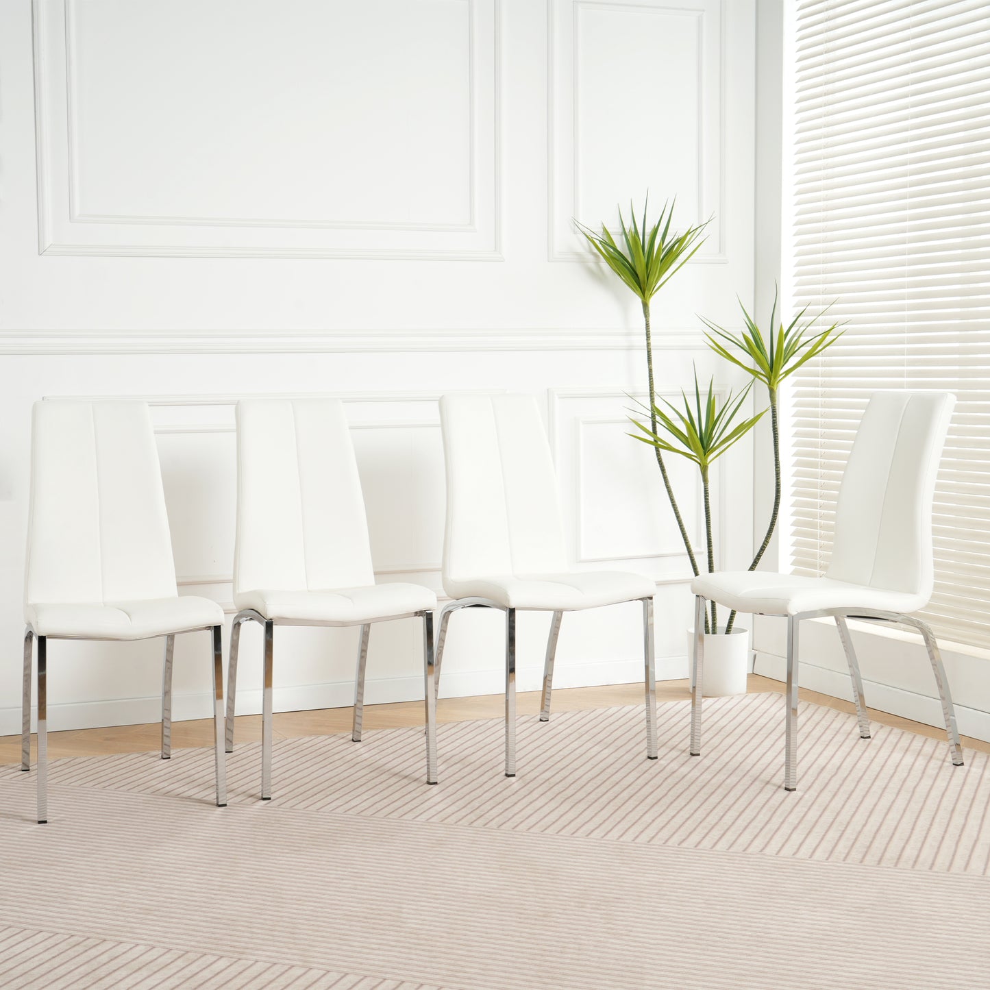 Four white faux leather dining chairs with chrome legs arranged in a dining room
