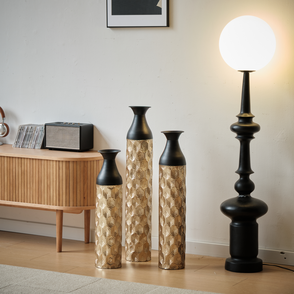 Three tall gold honeycomb ceramic vases with black tops arranged in a modern living room