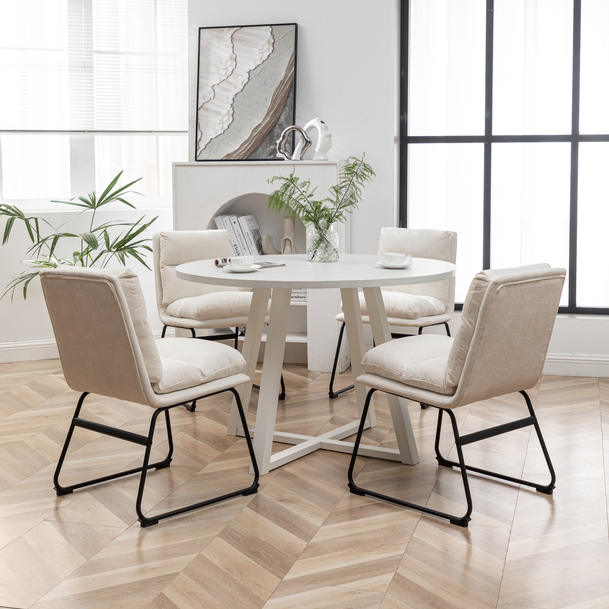 Round white dining table with four beige upholstered chairs with black metal legs