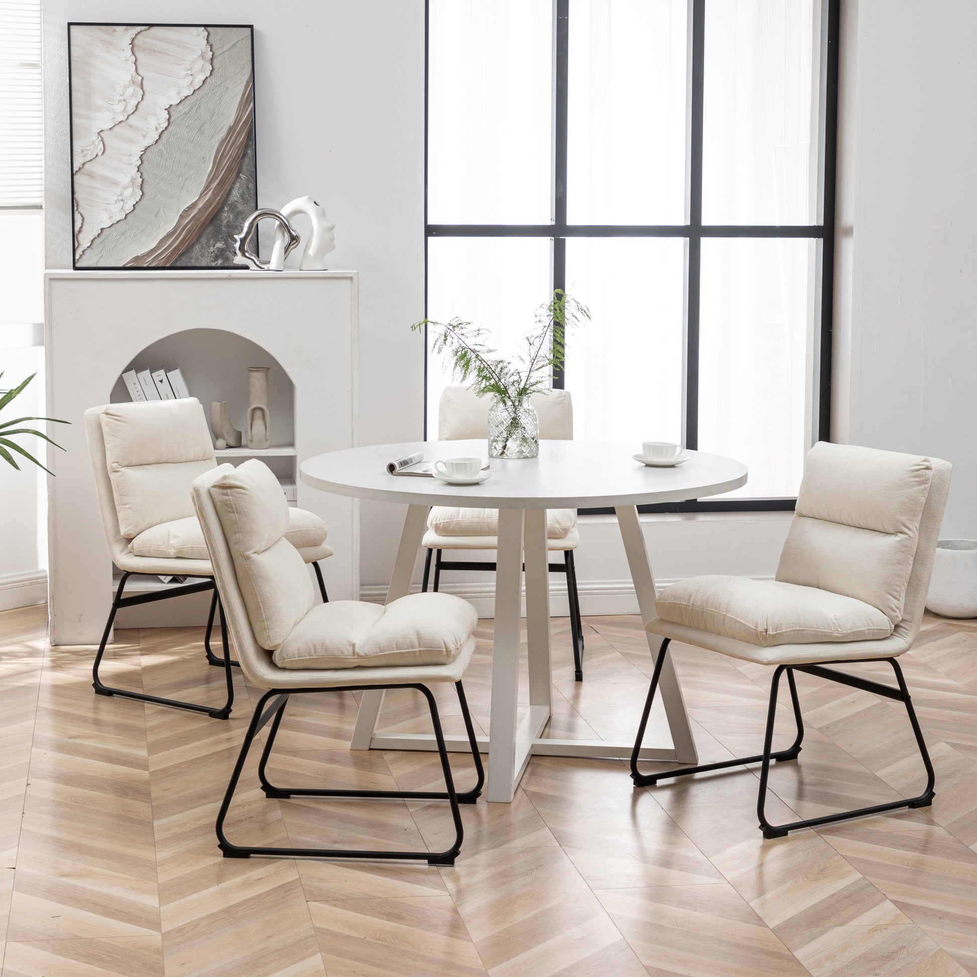 Four cream upholstered dining chairs with black metal legs around a white round table
