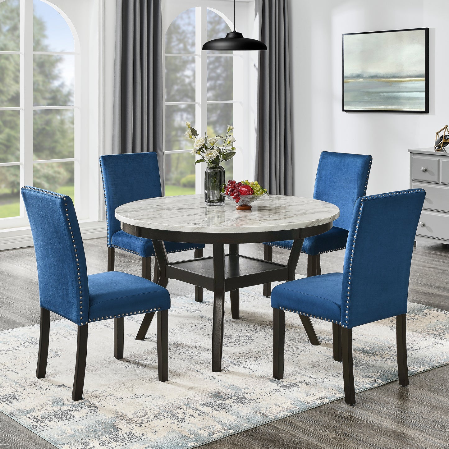 Round marble top dining table with dark wood base and four blue velvet dining chairs with silver nailhead trim